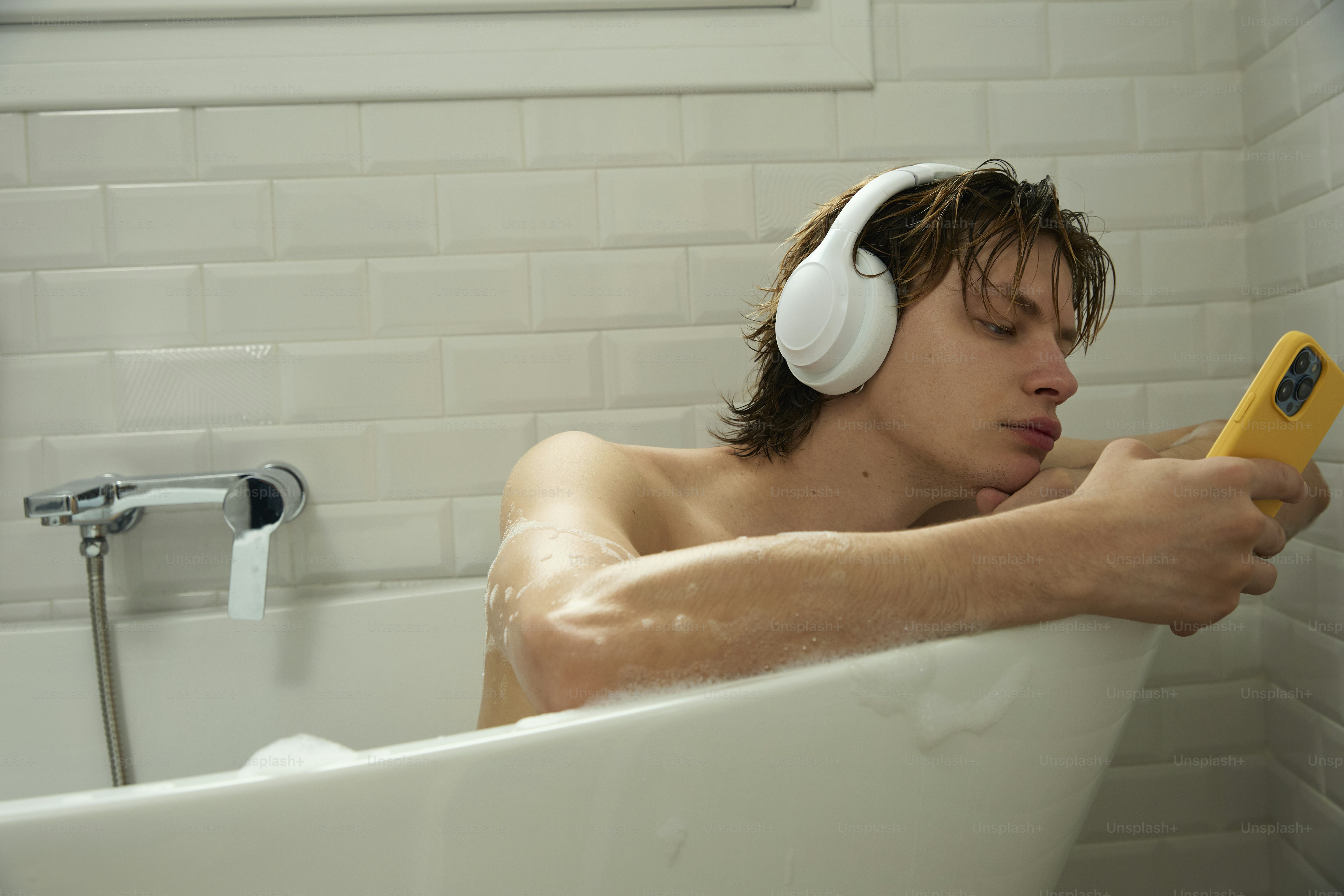 Man bathes, listens to music, and uses his phone.
