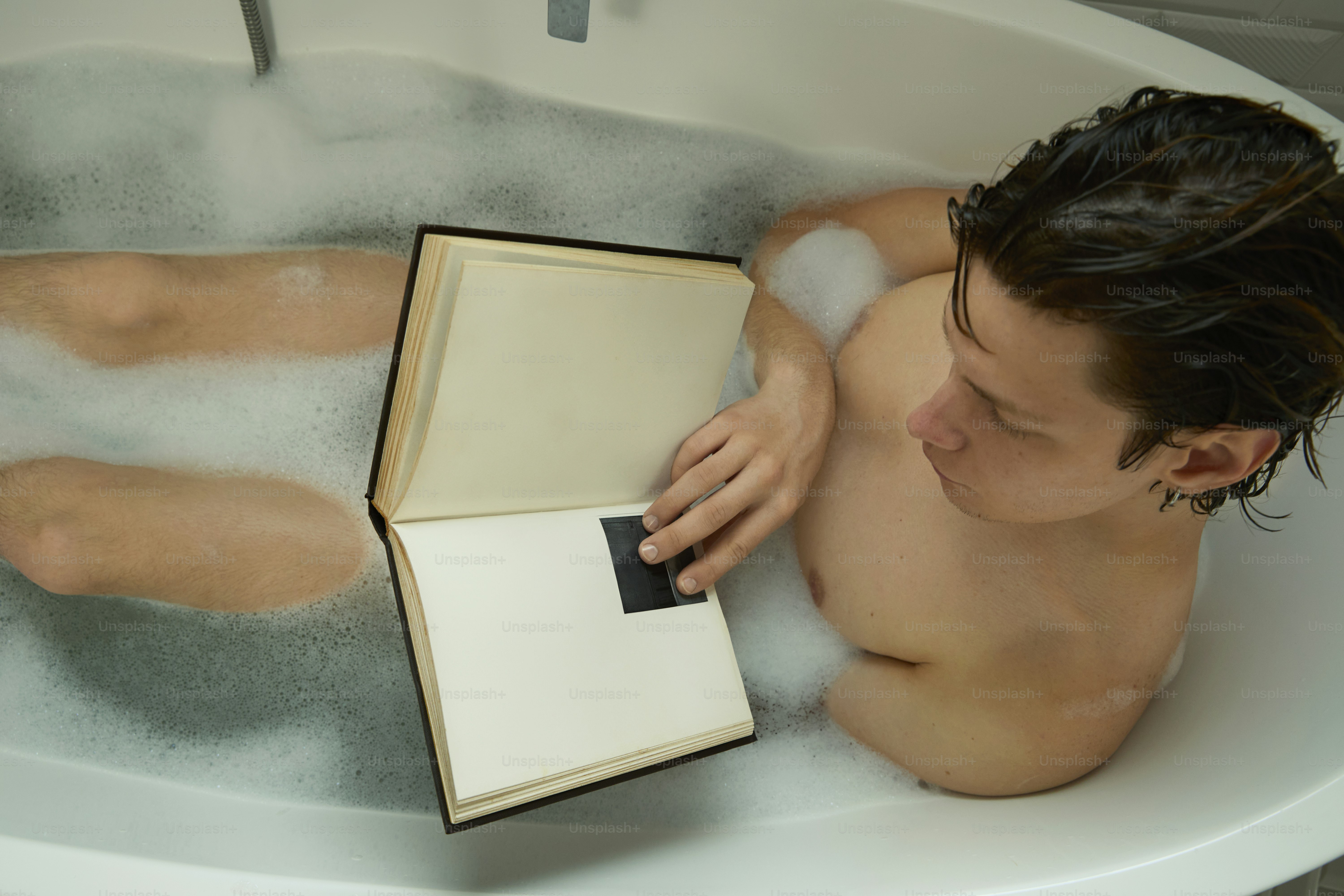 Man relaxes in a bubble bath while reading.