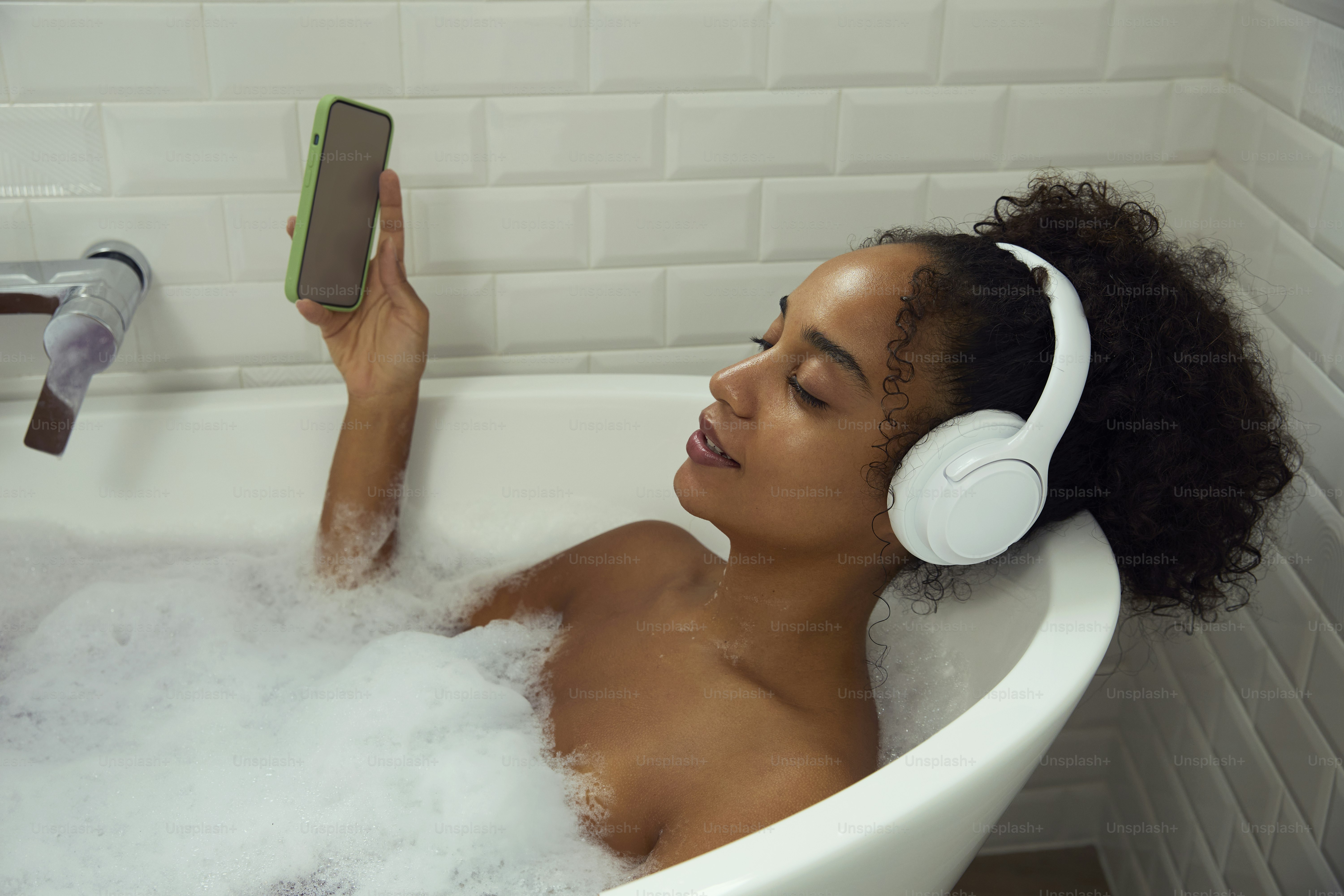 Die Frau hört Musik, während sie sich in einem Schaumbad entspannt.