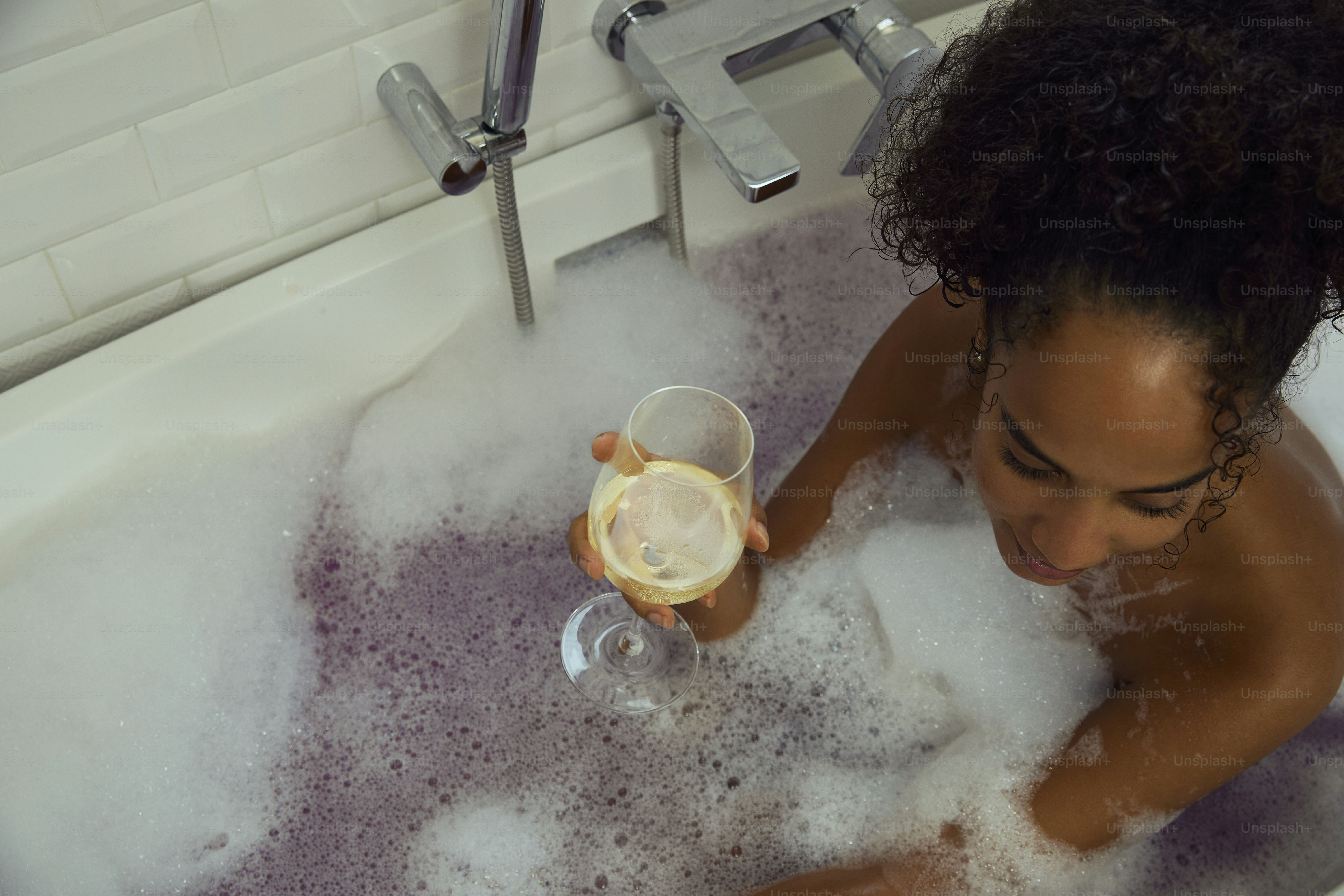 Woman enjoys a relaxing bath with a glass of wine.
