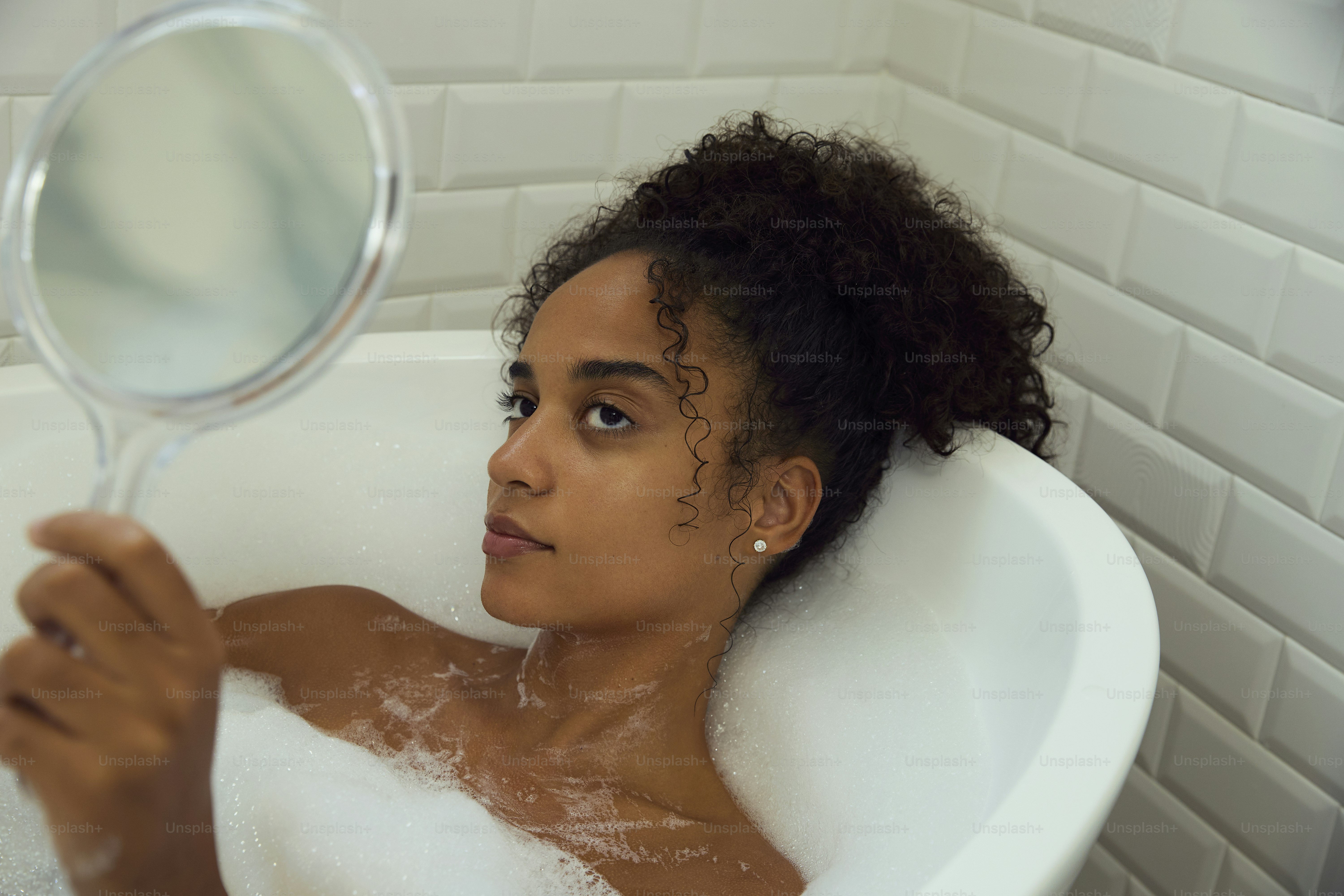 Frau entspannt sich in einer Badewanne und schaut in einen Spiegel.