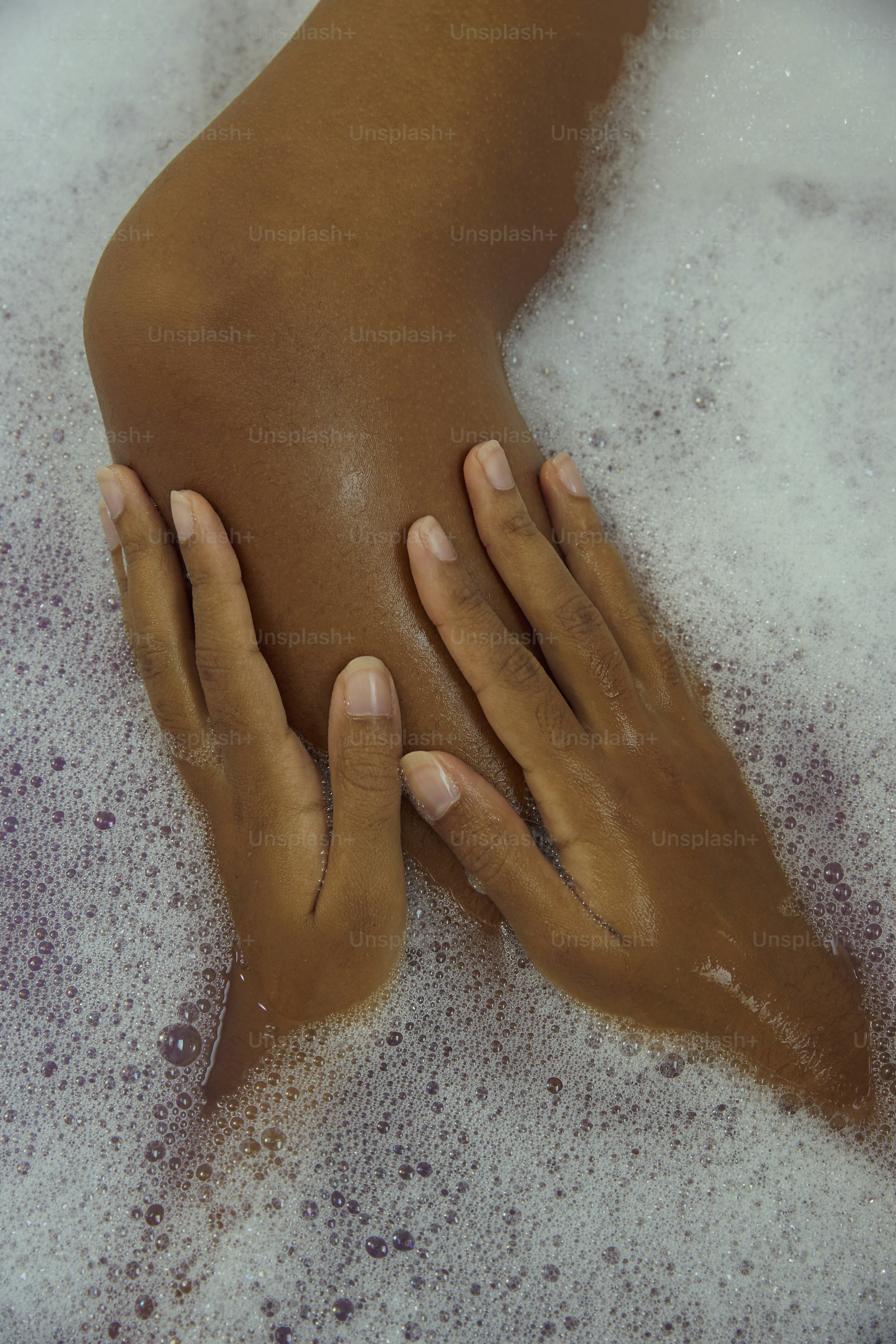 Eine Hand berührt sanft ein Bein mit Seifenwasser.
