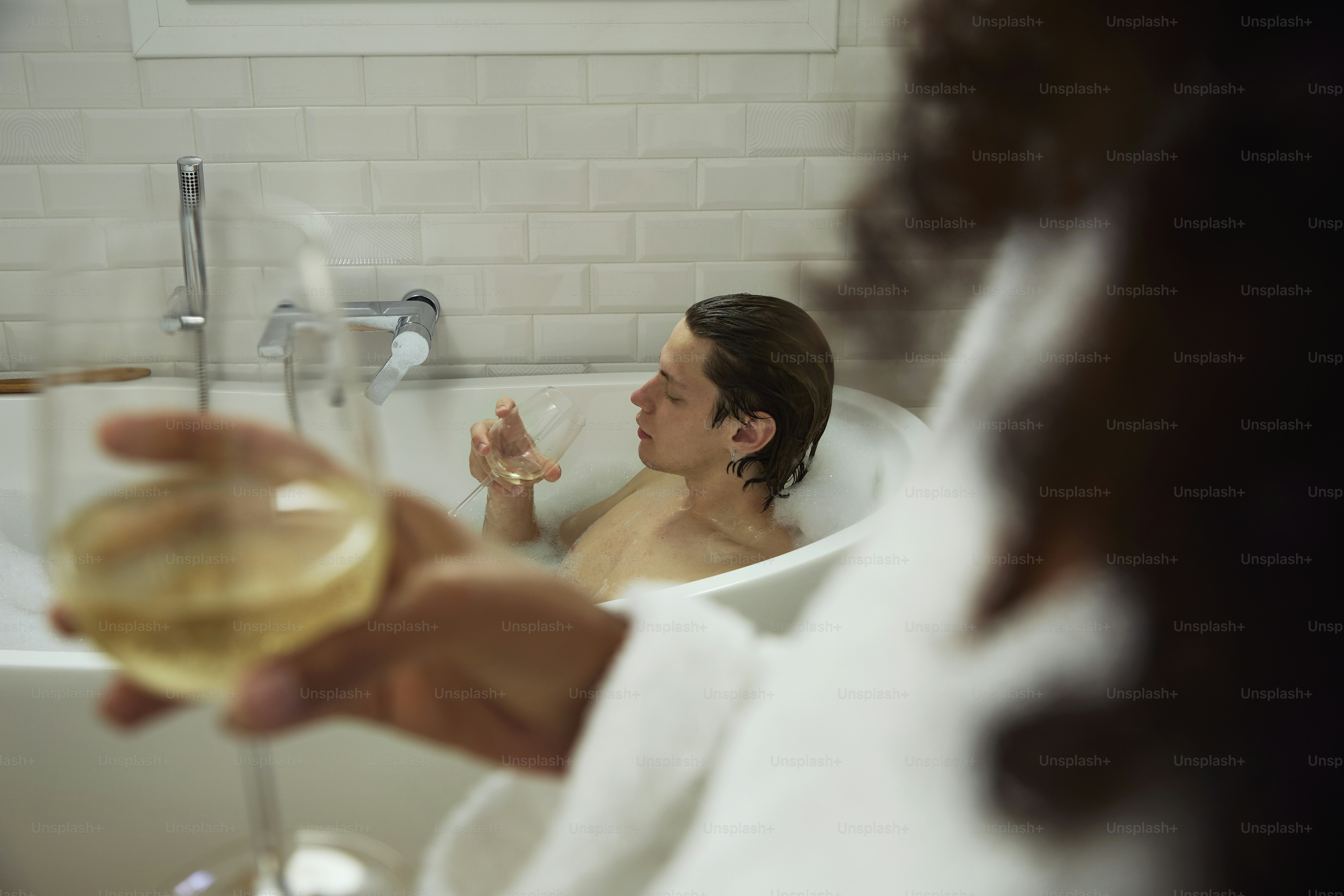 Someone enjoys wine while relaxing in a bathtub.