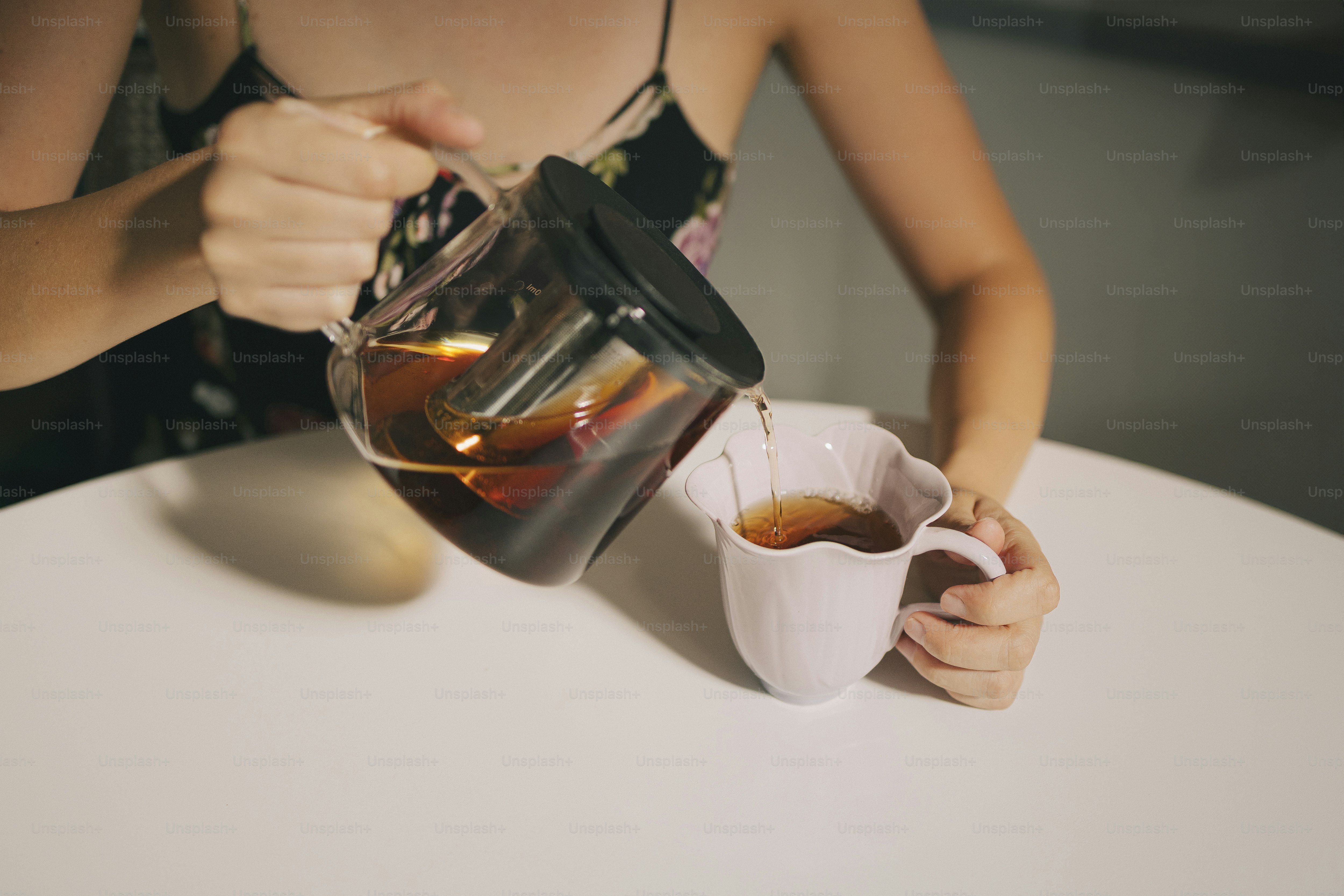 A person pours tea from a glass teapot.