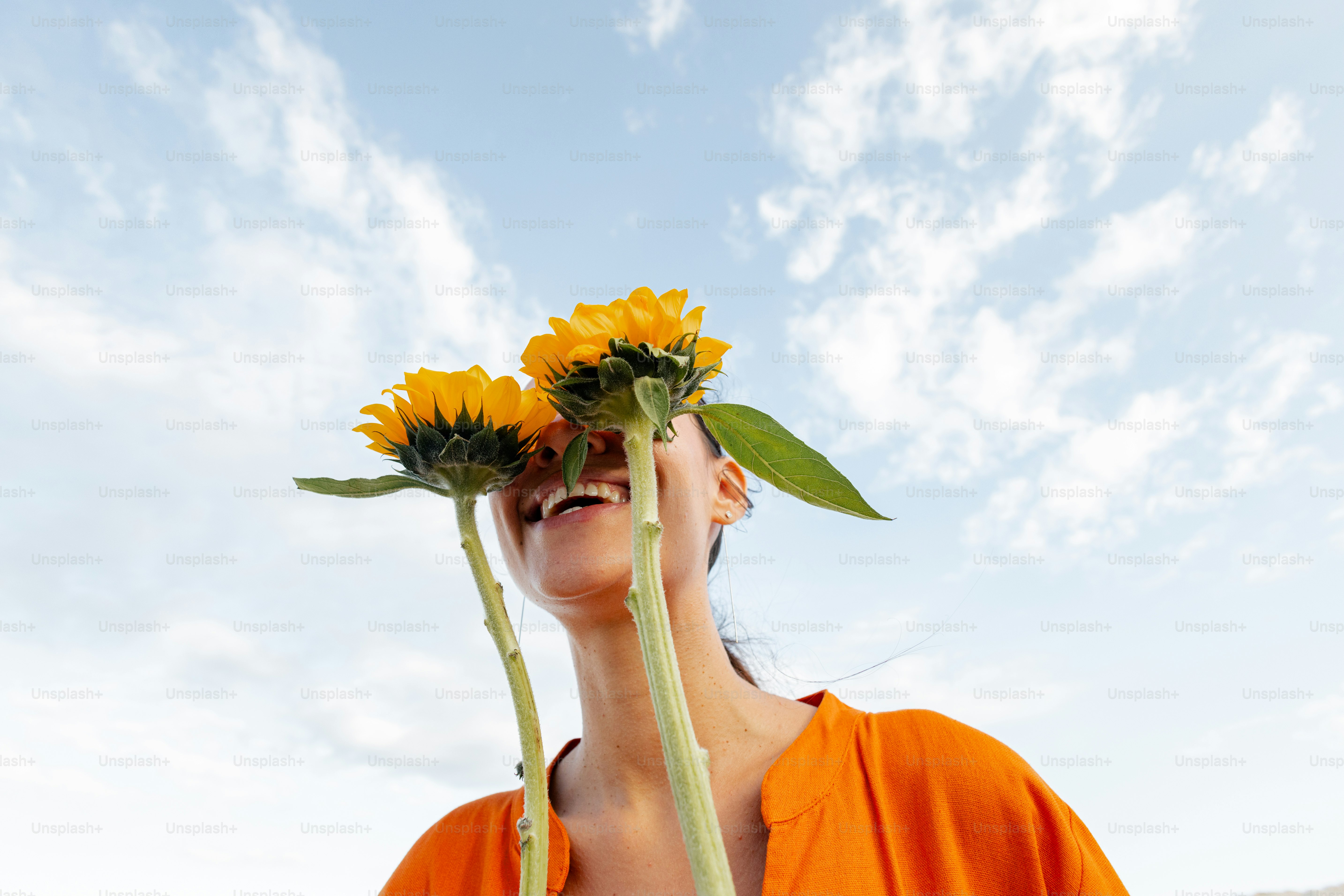 Woman hides behind sunflowers under a cloudy sky.