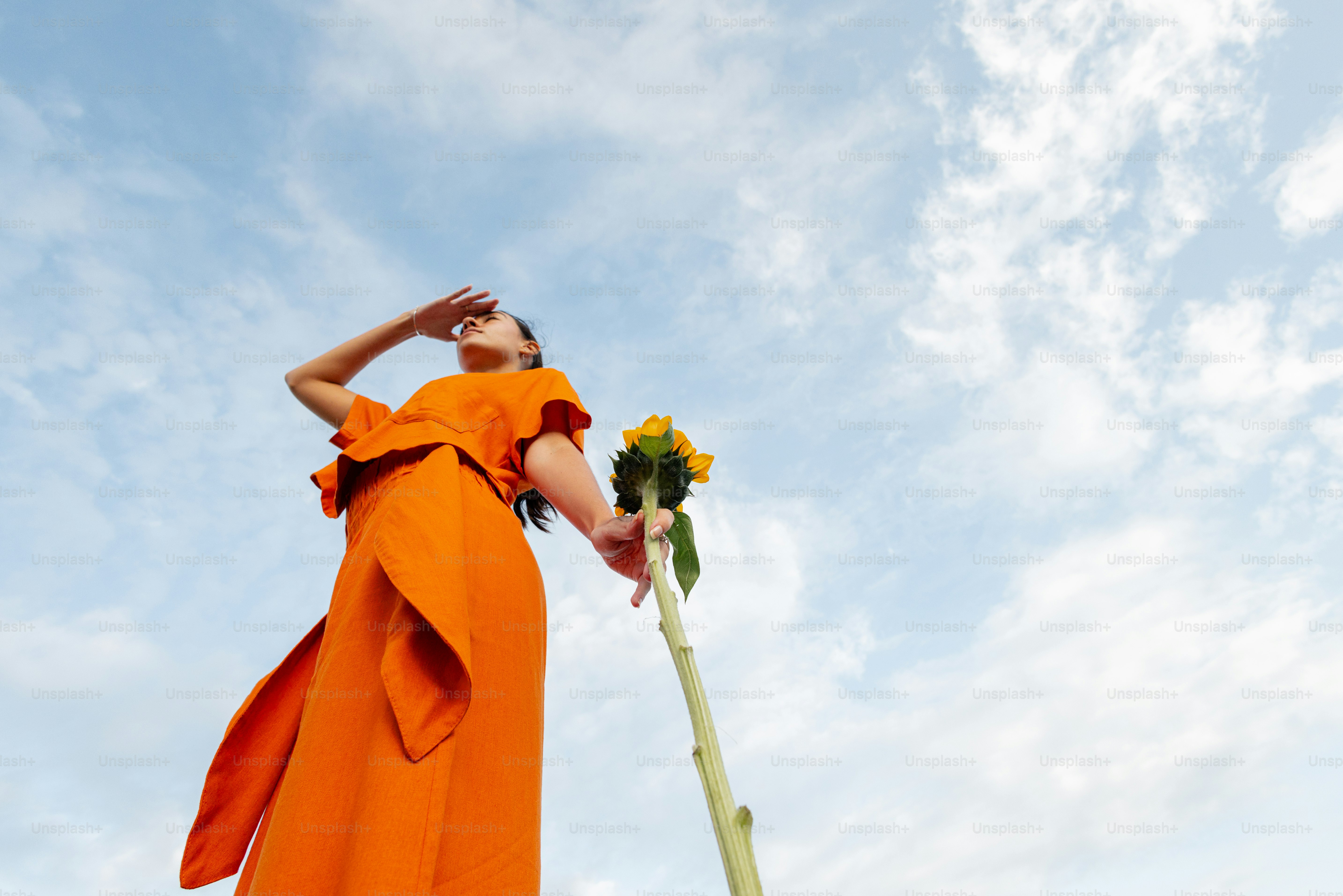 Woman in orange dress looks up at the sky.