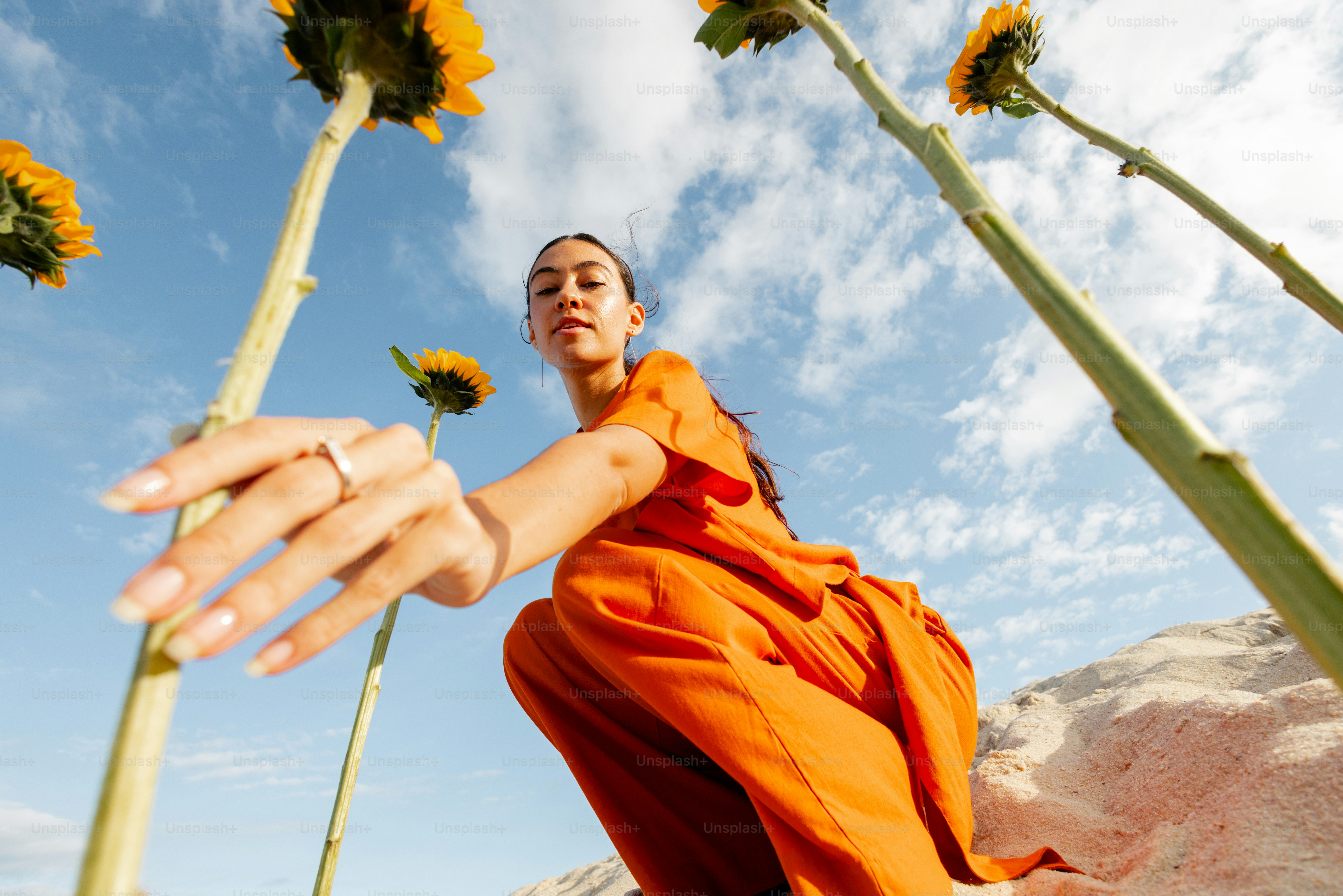Woman in orange dress poses with sunflowers.