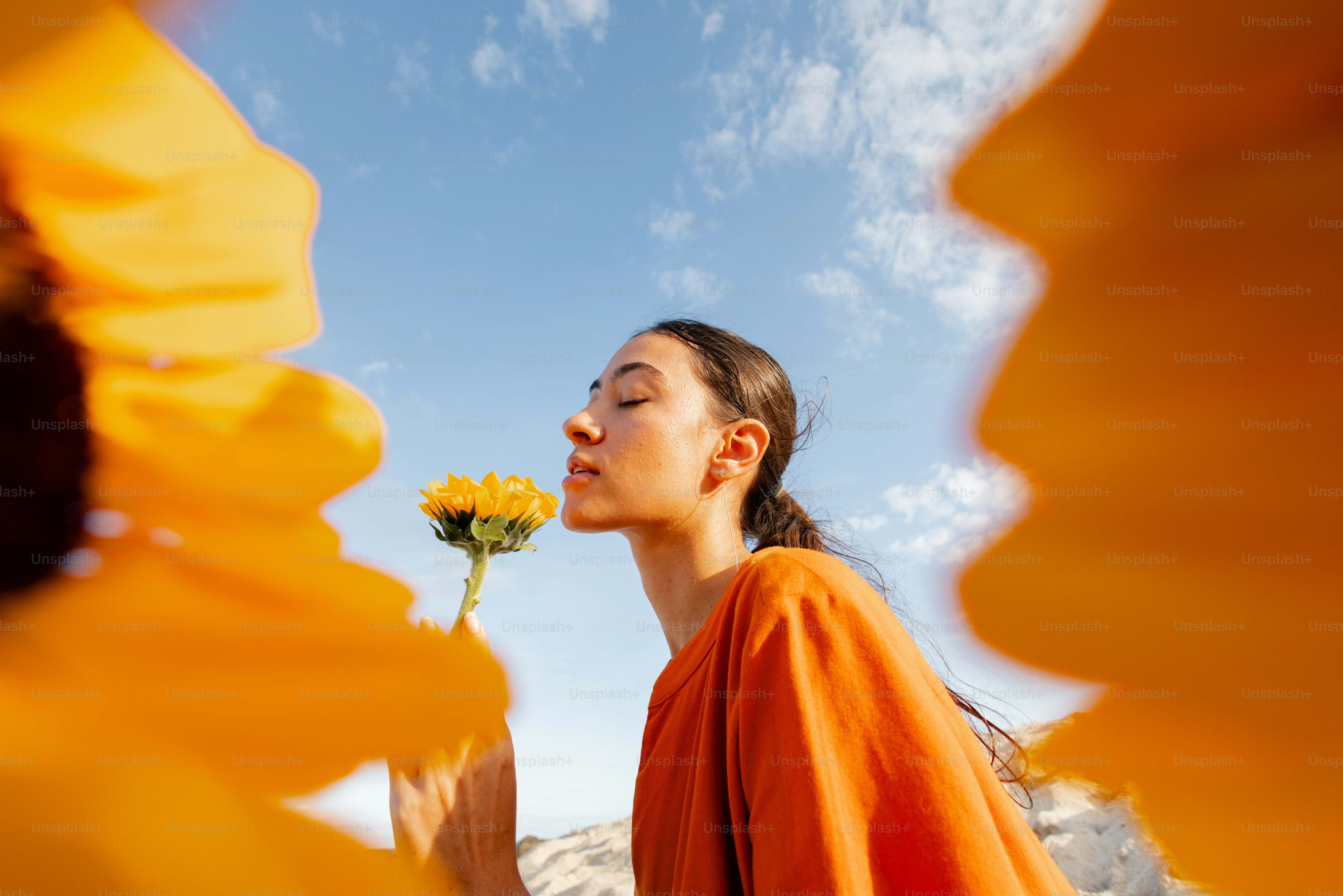 Woman smelling a sunflower under a blue sky.