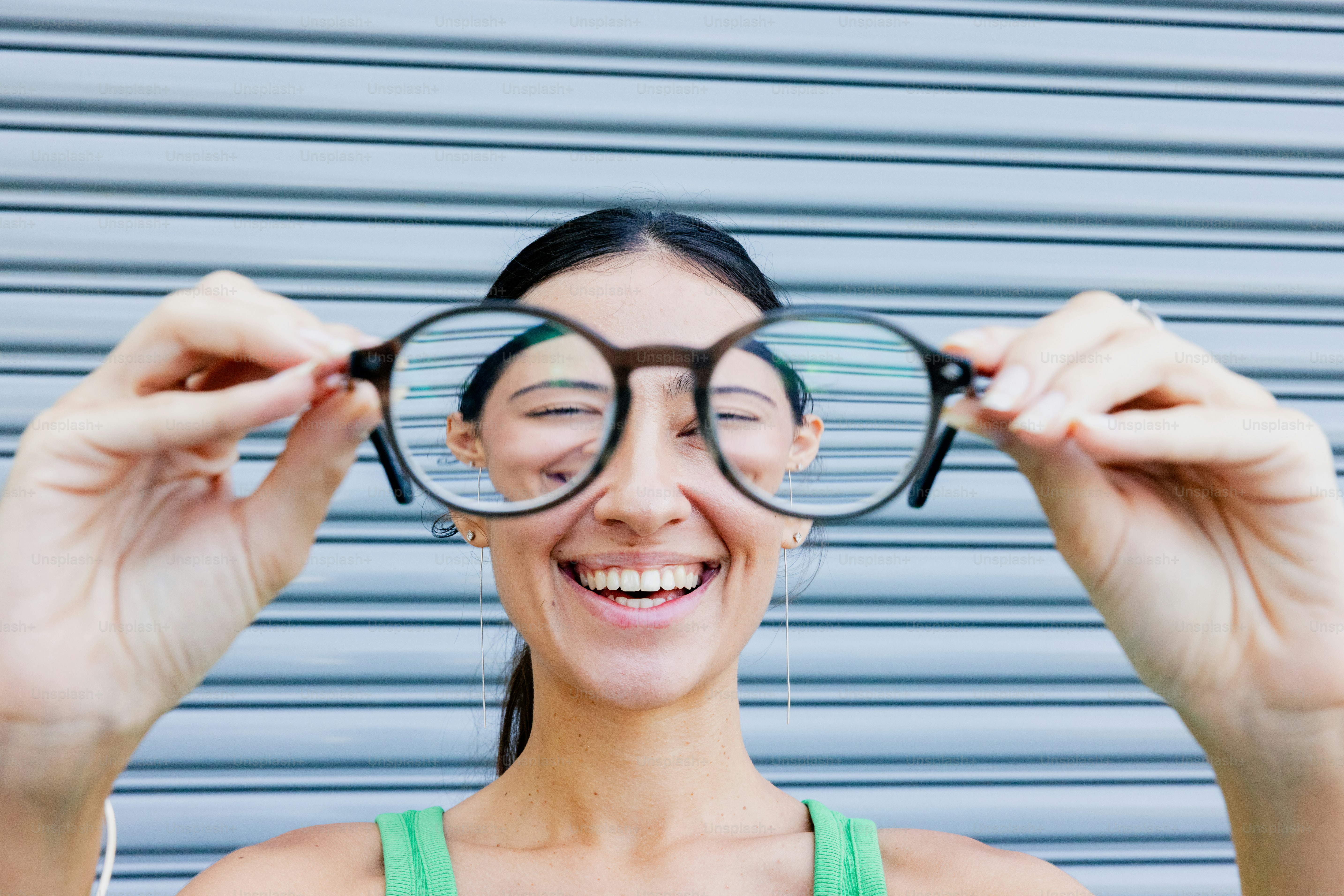 Woman holds up oversized glasses, smiling widely.