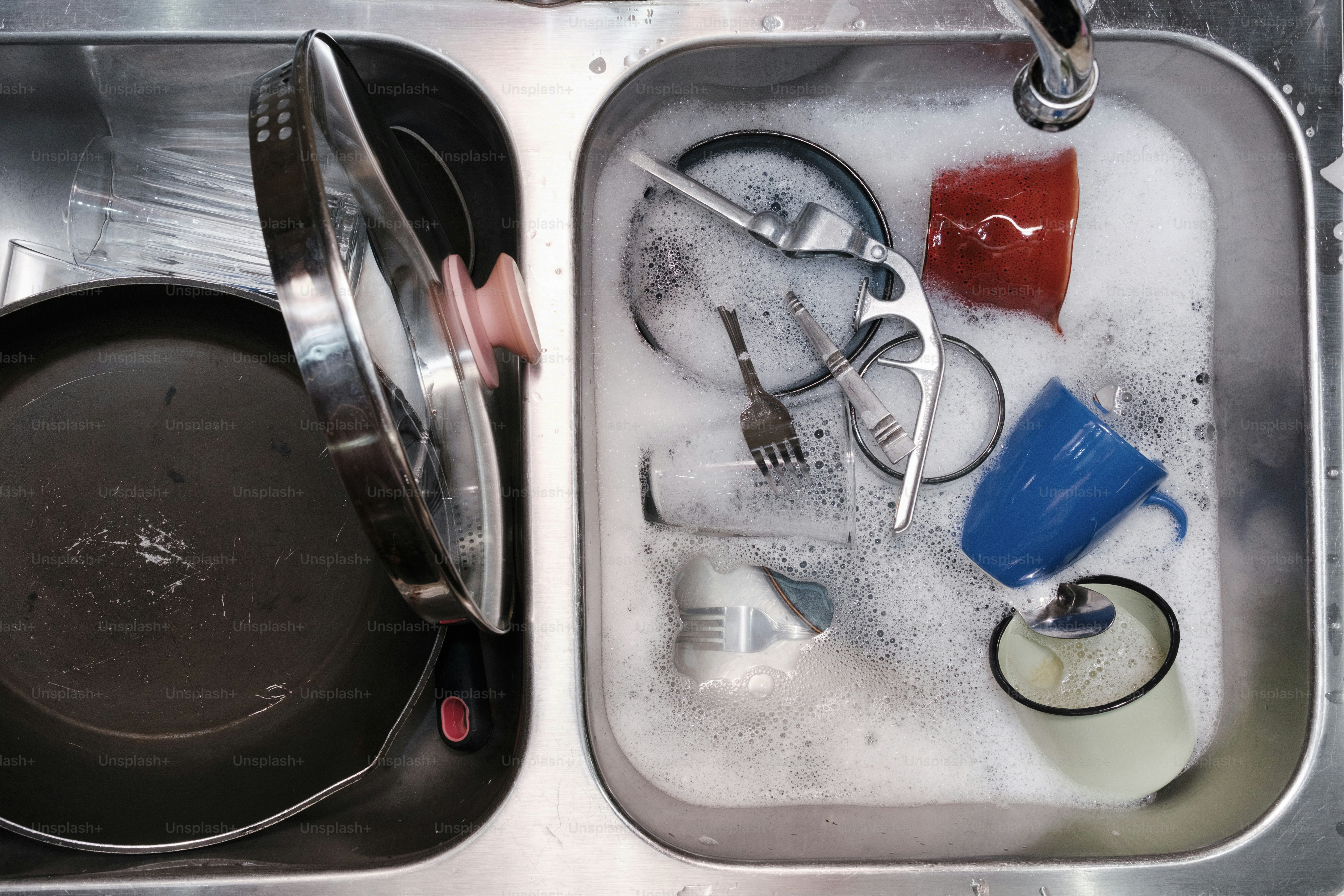 Dirty dishes are soaking in a soapy sink.