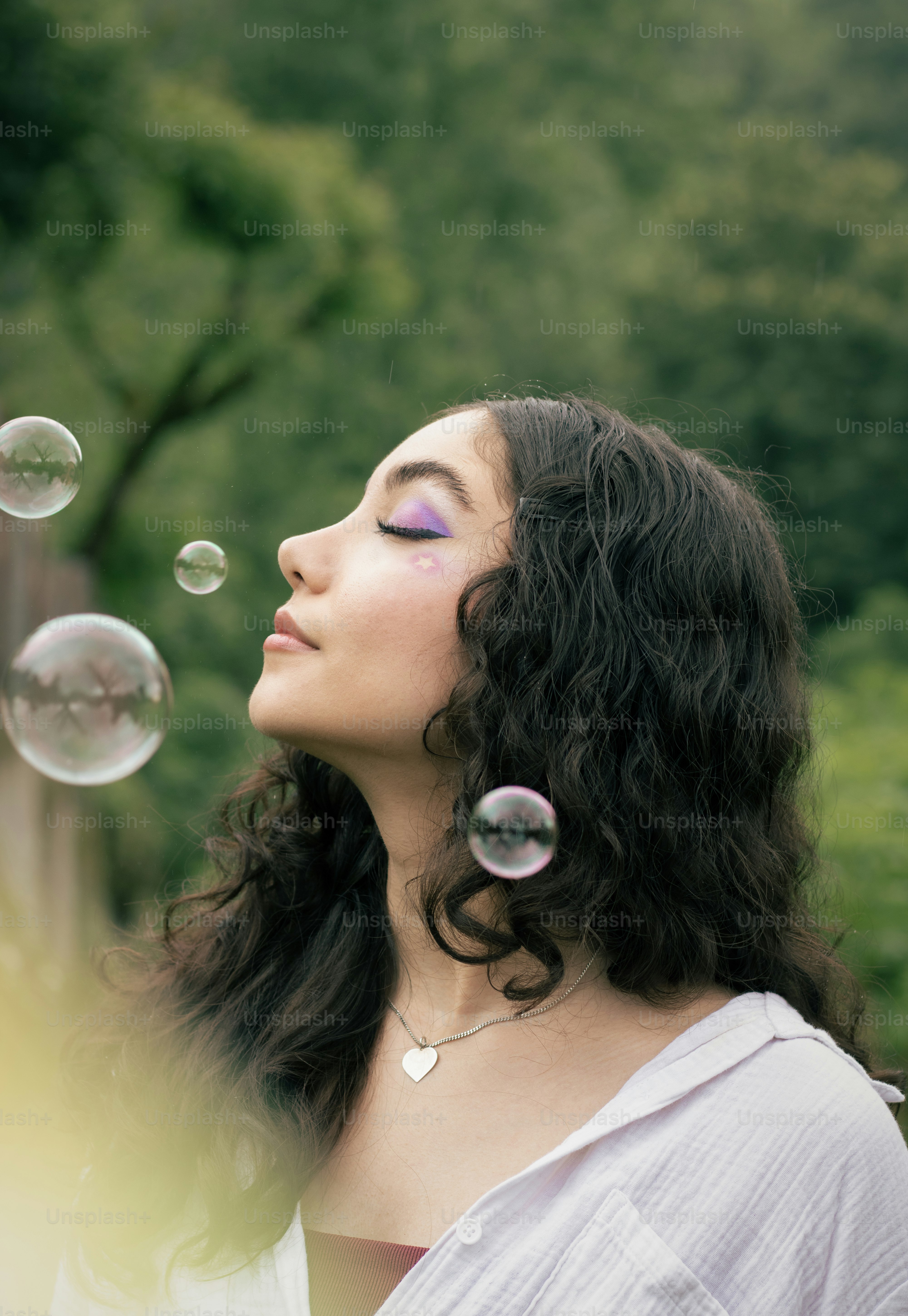 Woman enjoys bubbles with eyes closed in nature.