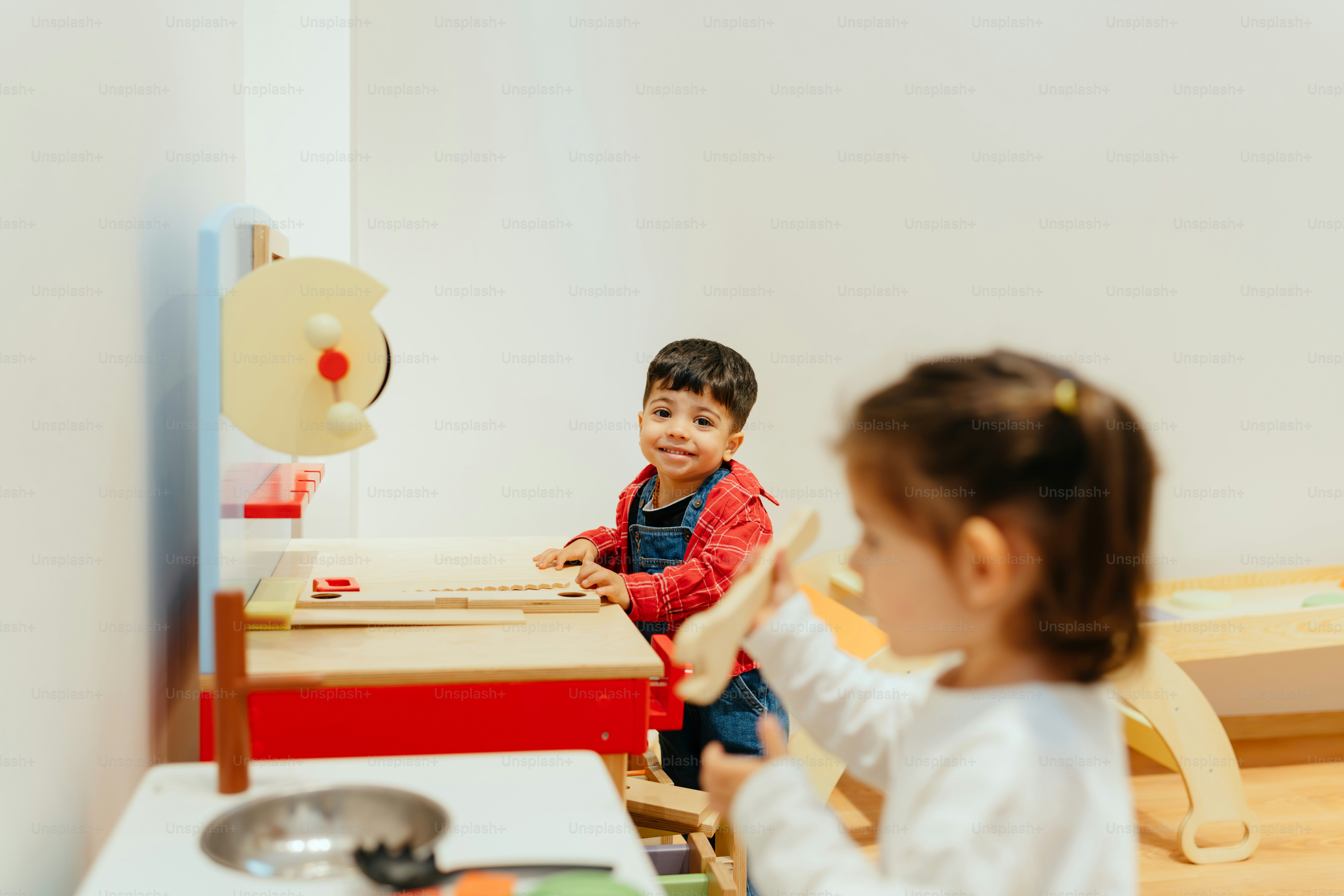 Children play in a toy kitchen, smiling happily.