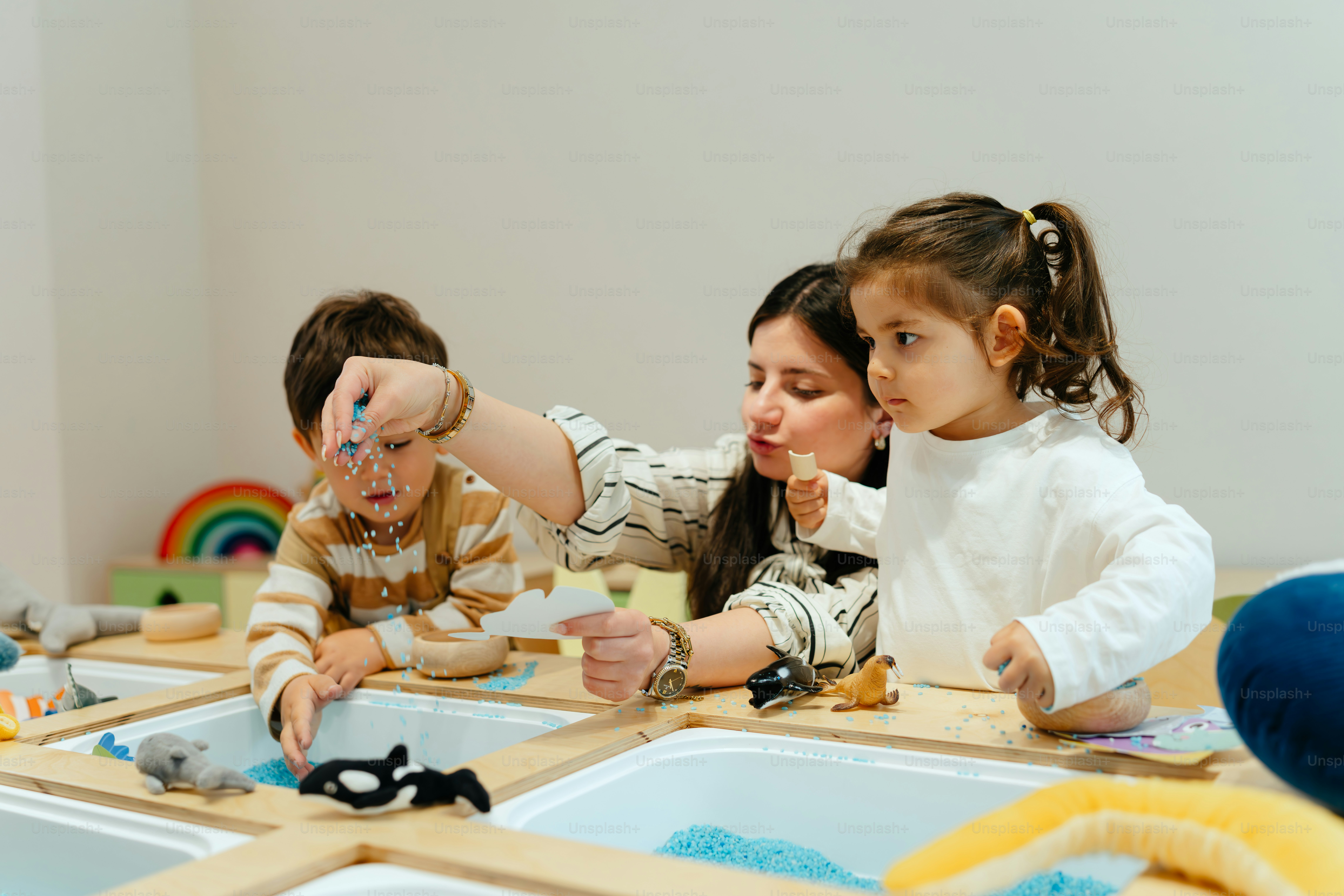 Teacher and children play with toy animals in water.