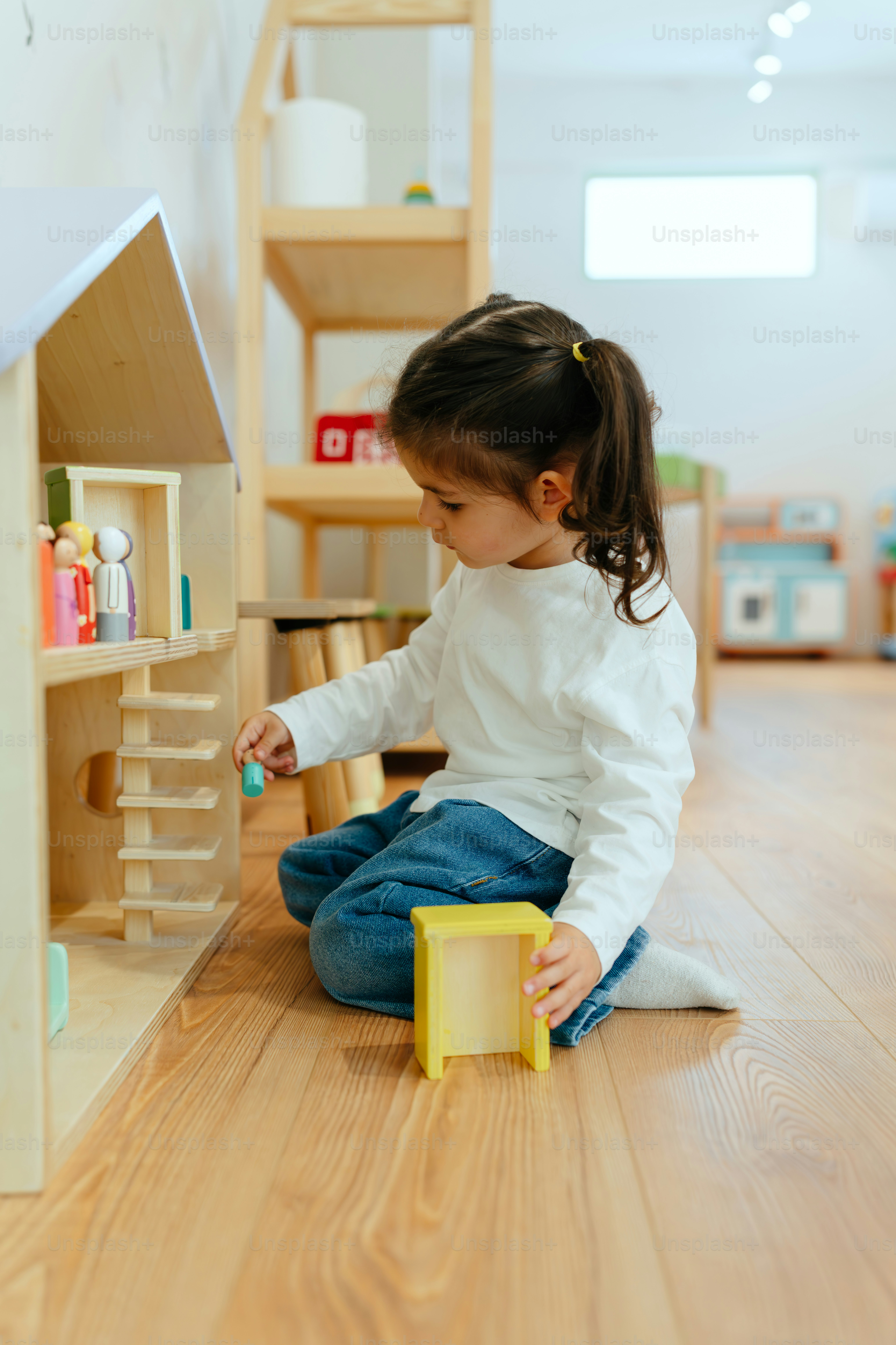 A little girl plays with a dollhouse.