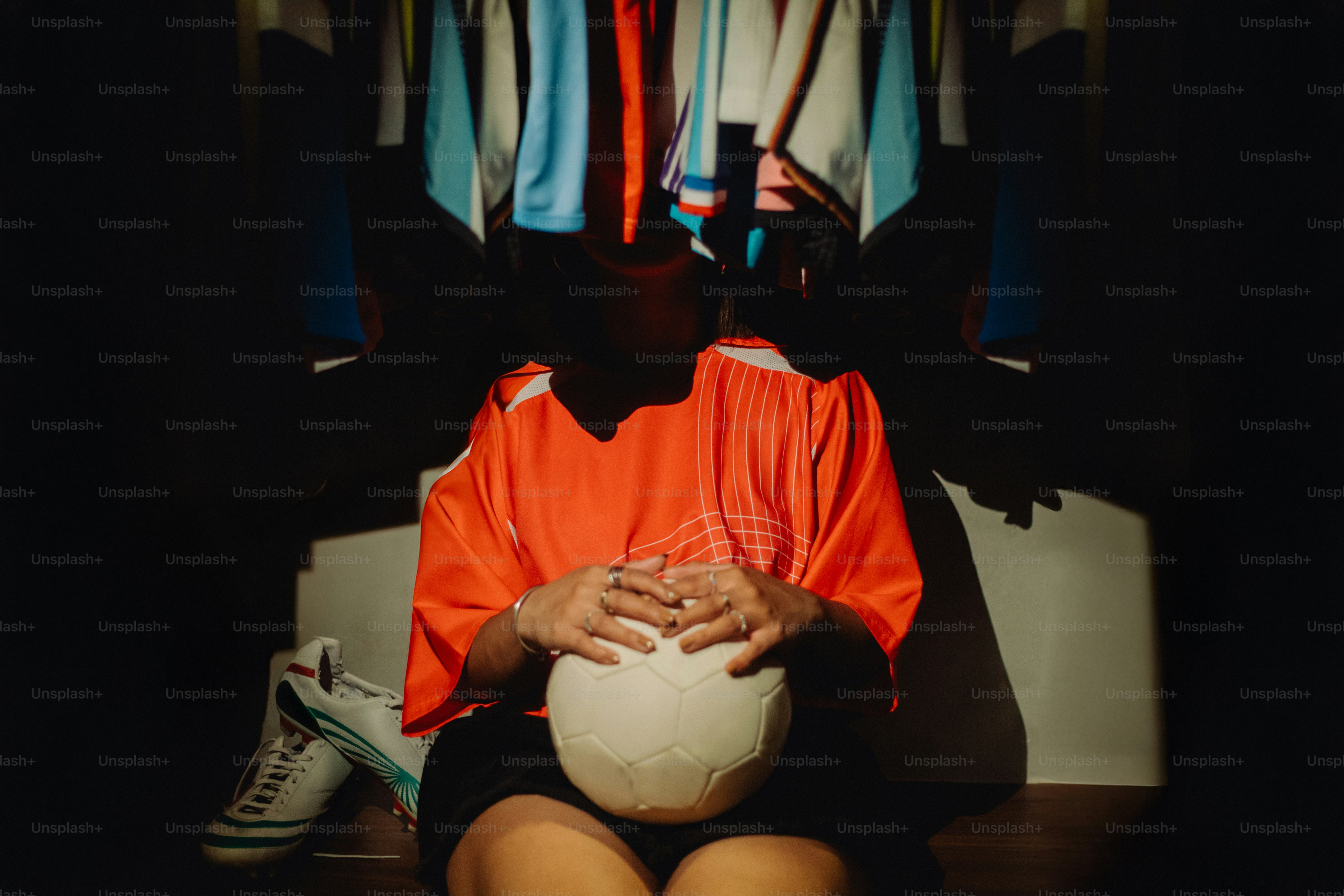 Pemain memegang bola sepak, dikelilingi oleh kaus.