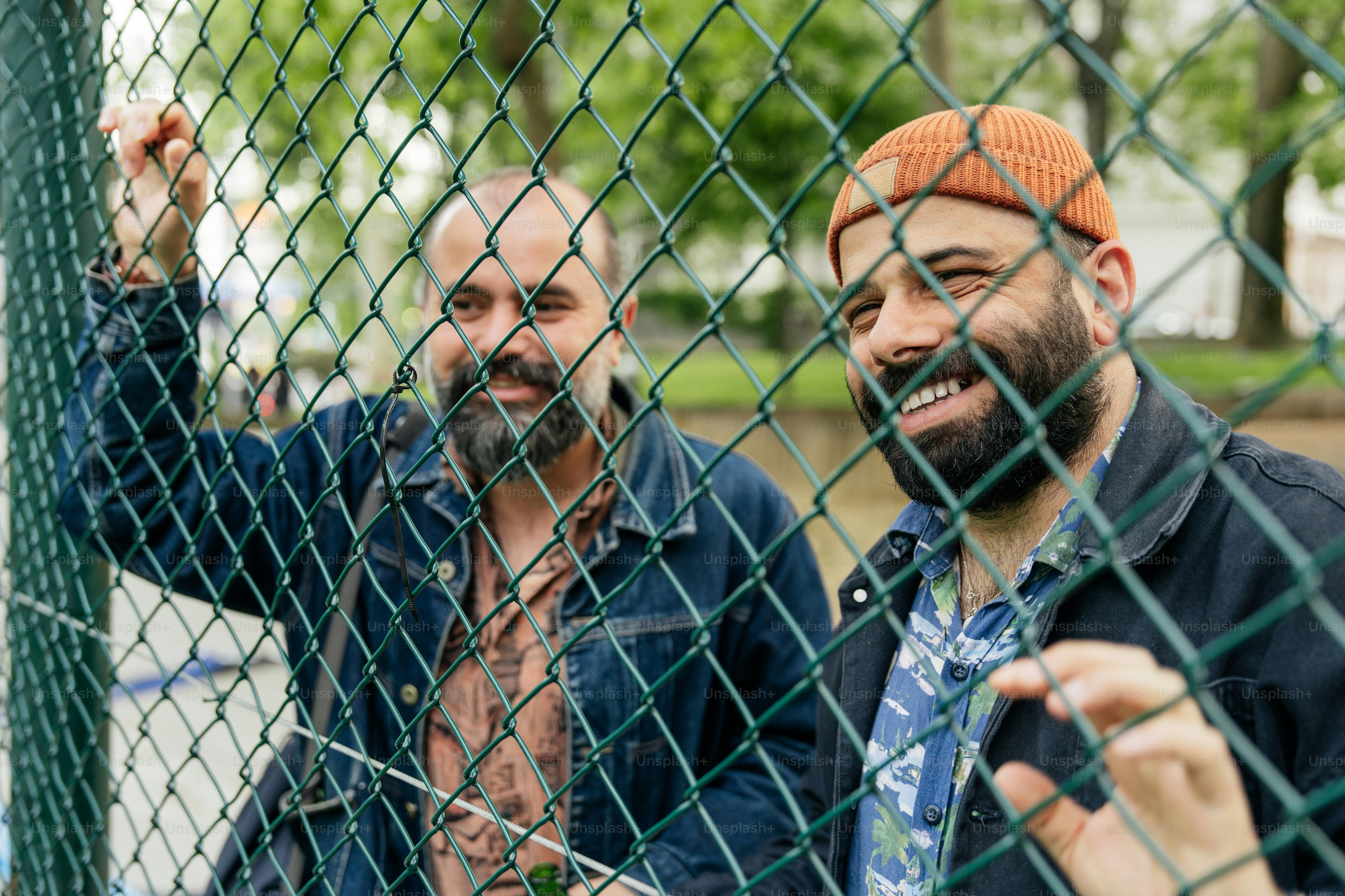Two smiling men behind a green fence.