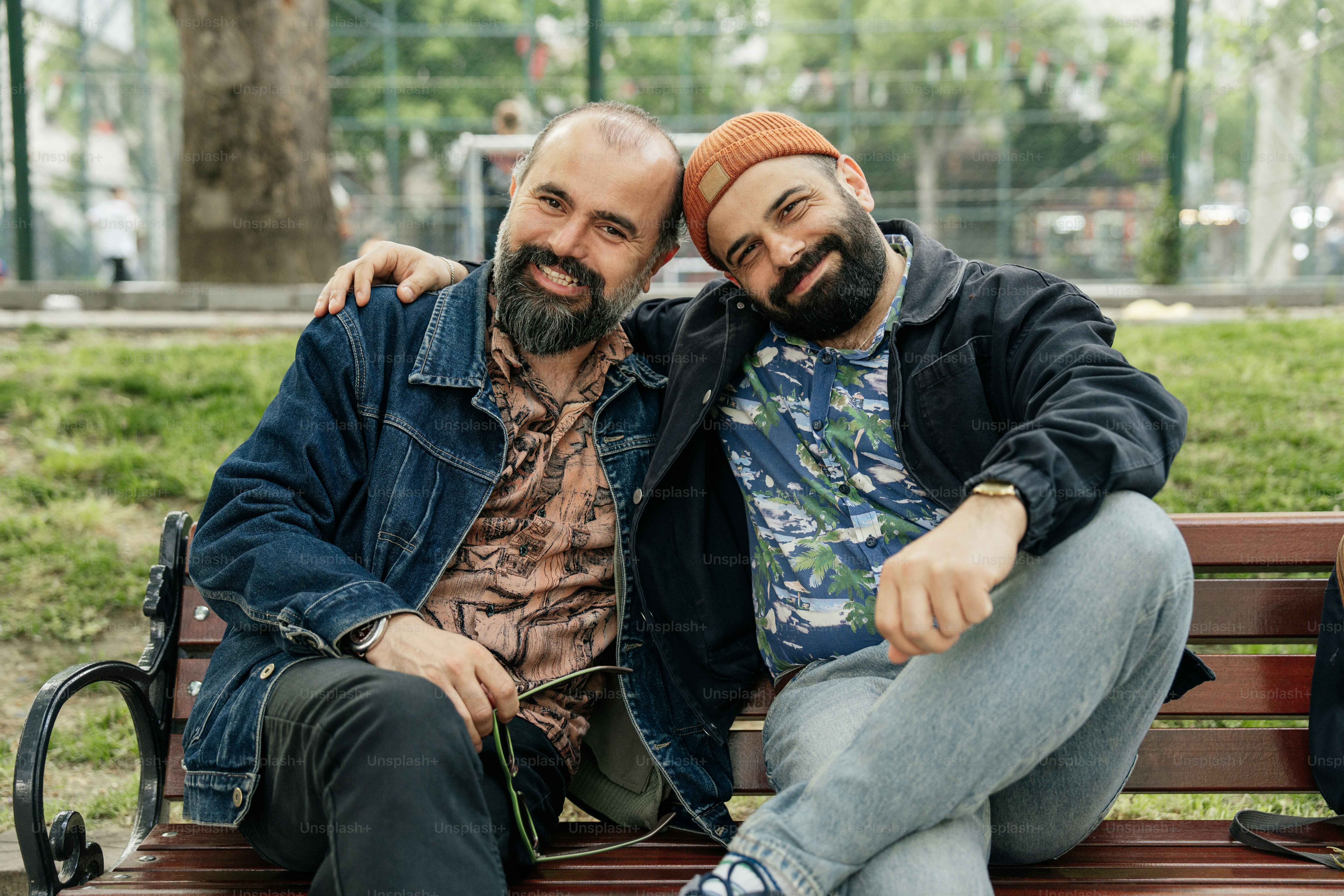 Two smiling men sit together on a bench.