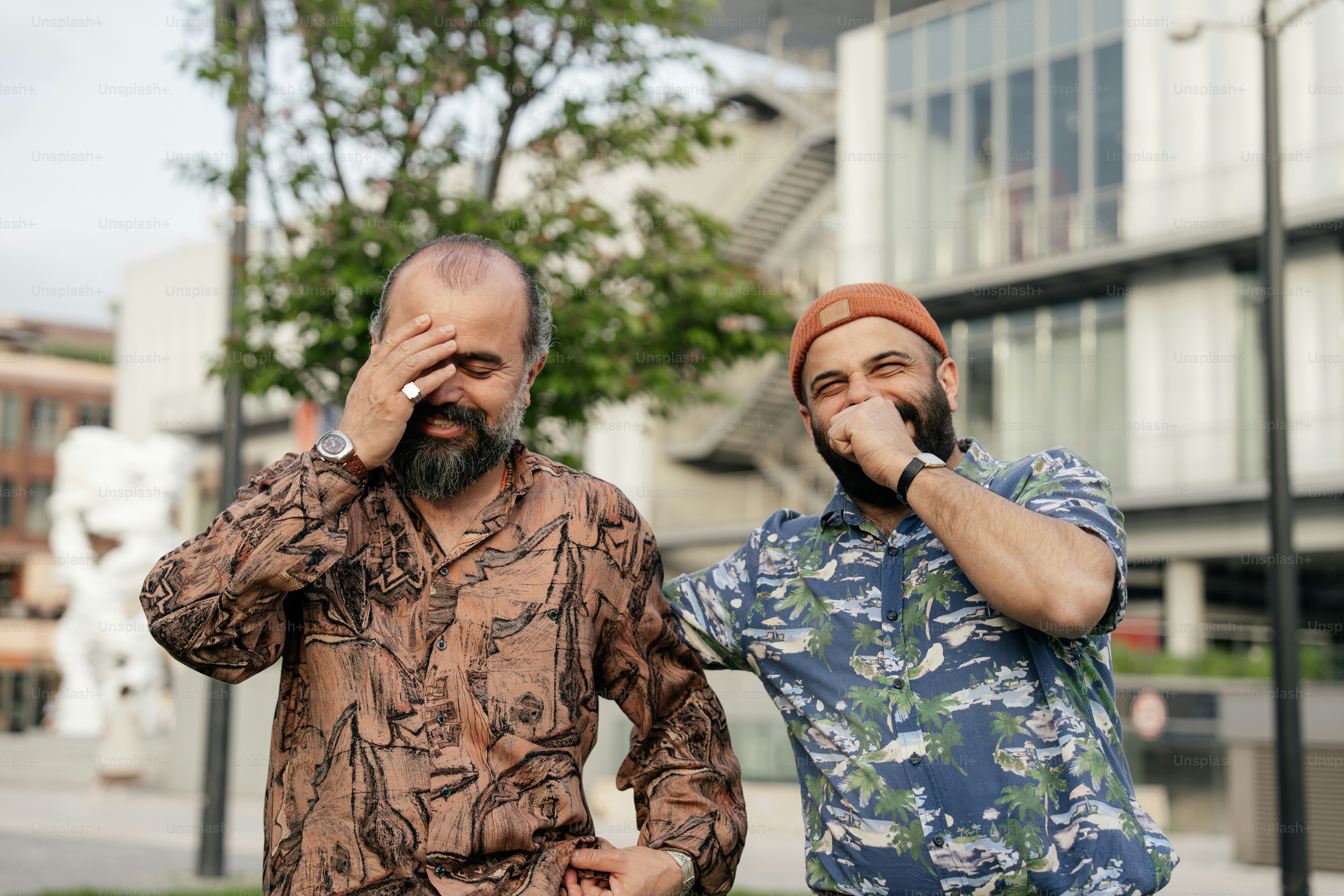 Zwei Männer lachen im Freien und bedecken ihre Gesichter.