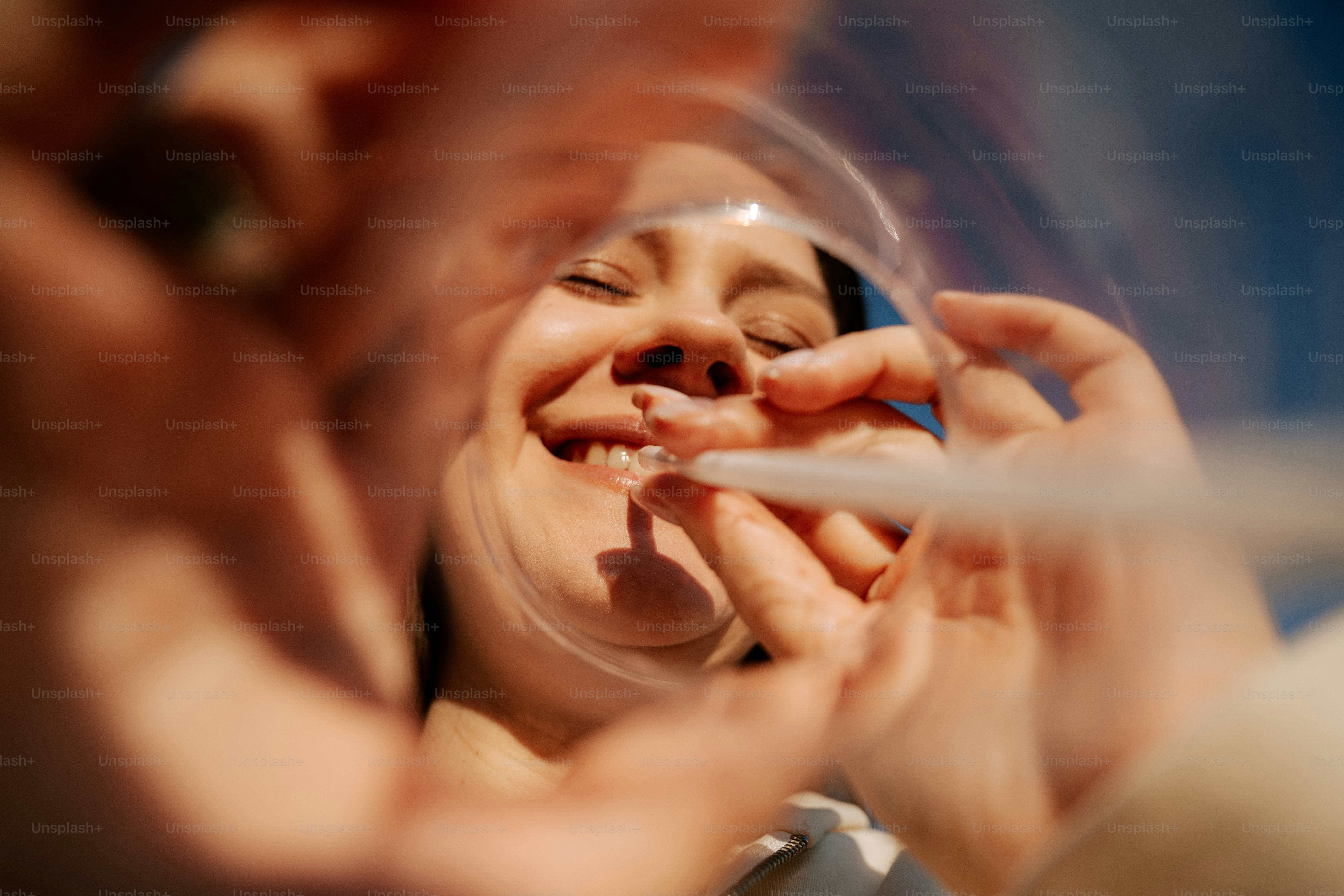 Woman is smiling as she applies something to her lip.
