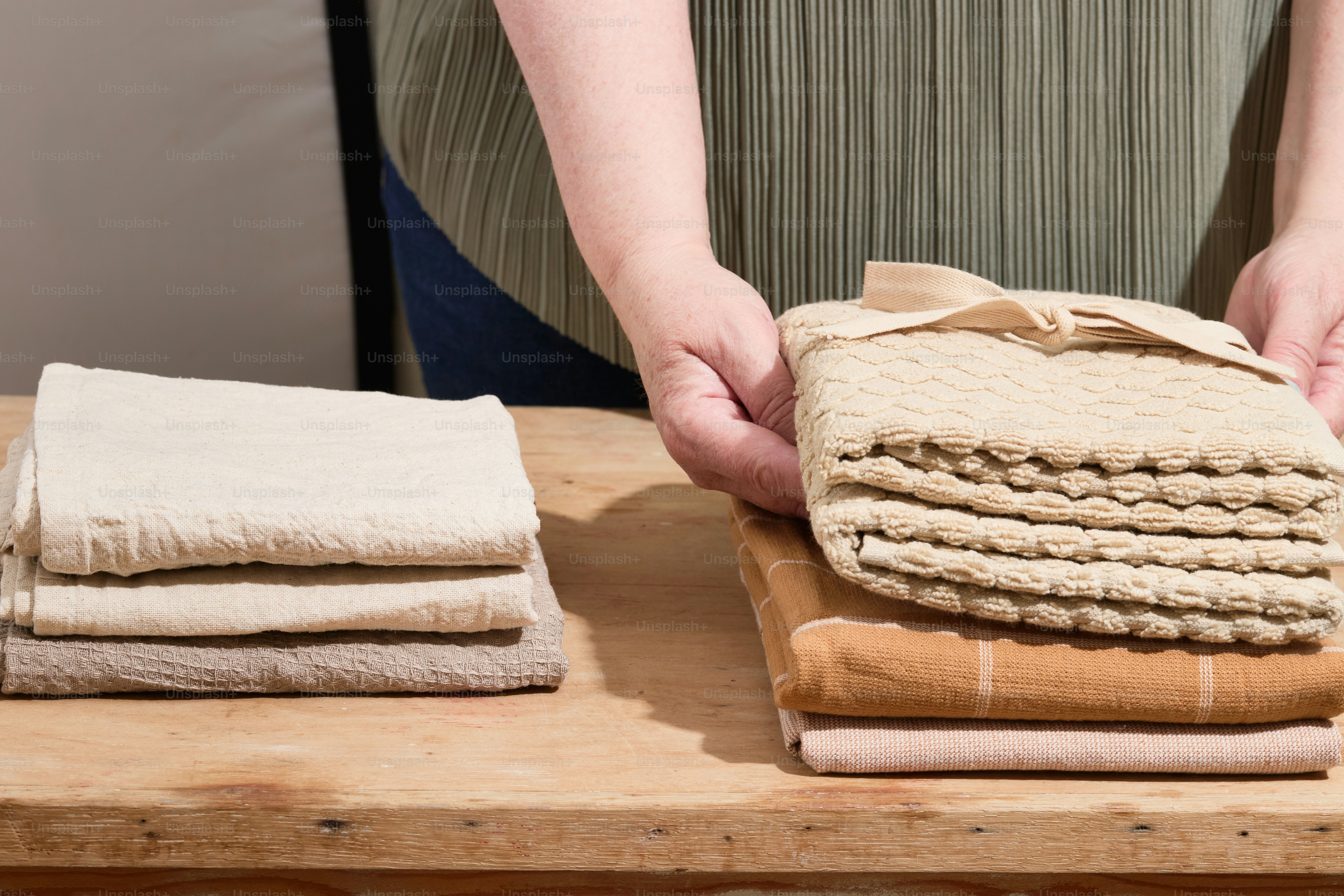 Person neatly arranges folded towels on a table.