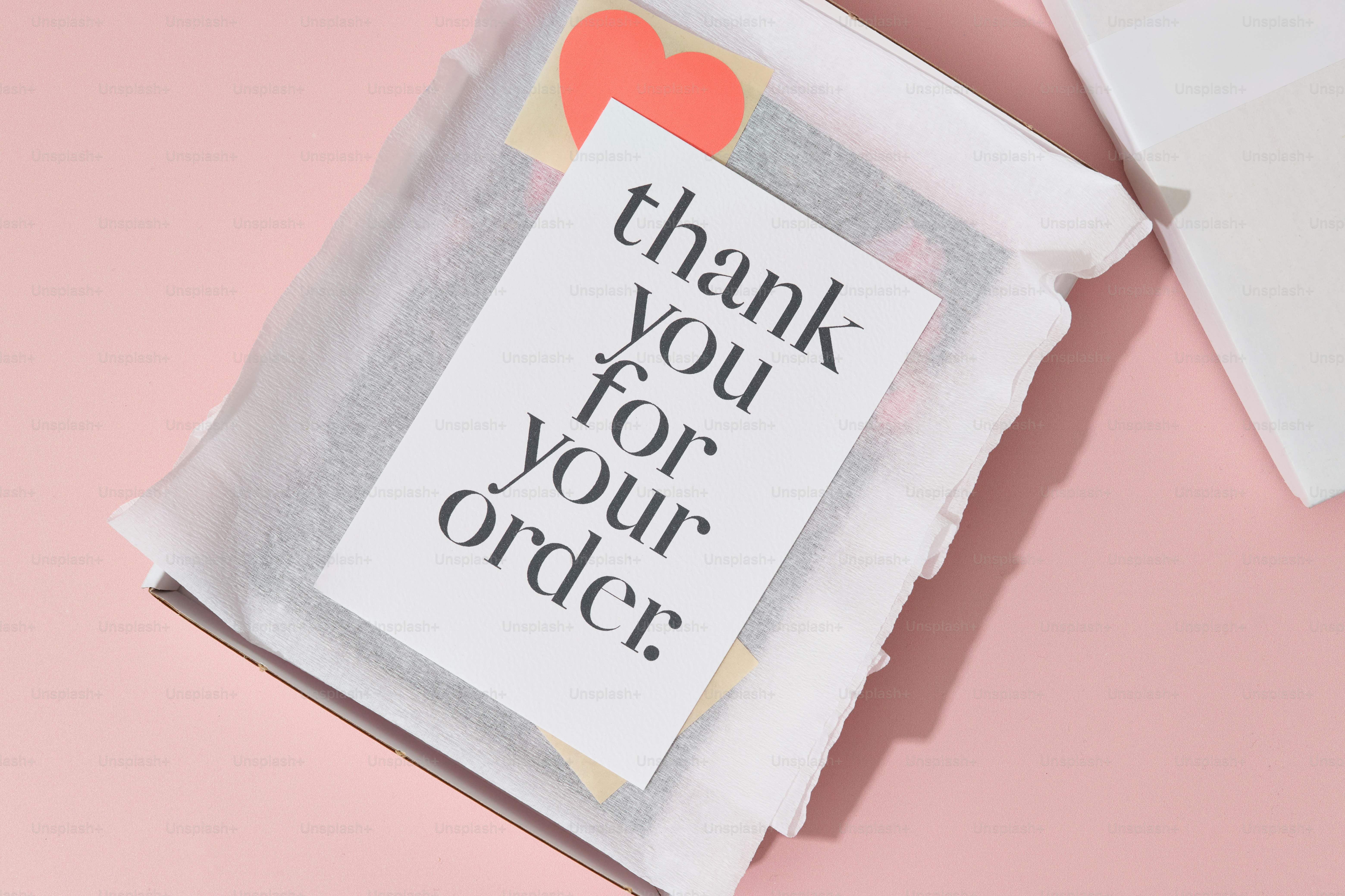 An online purchase in a shipping package with personal branding and accessories on a pink table.