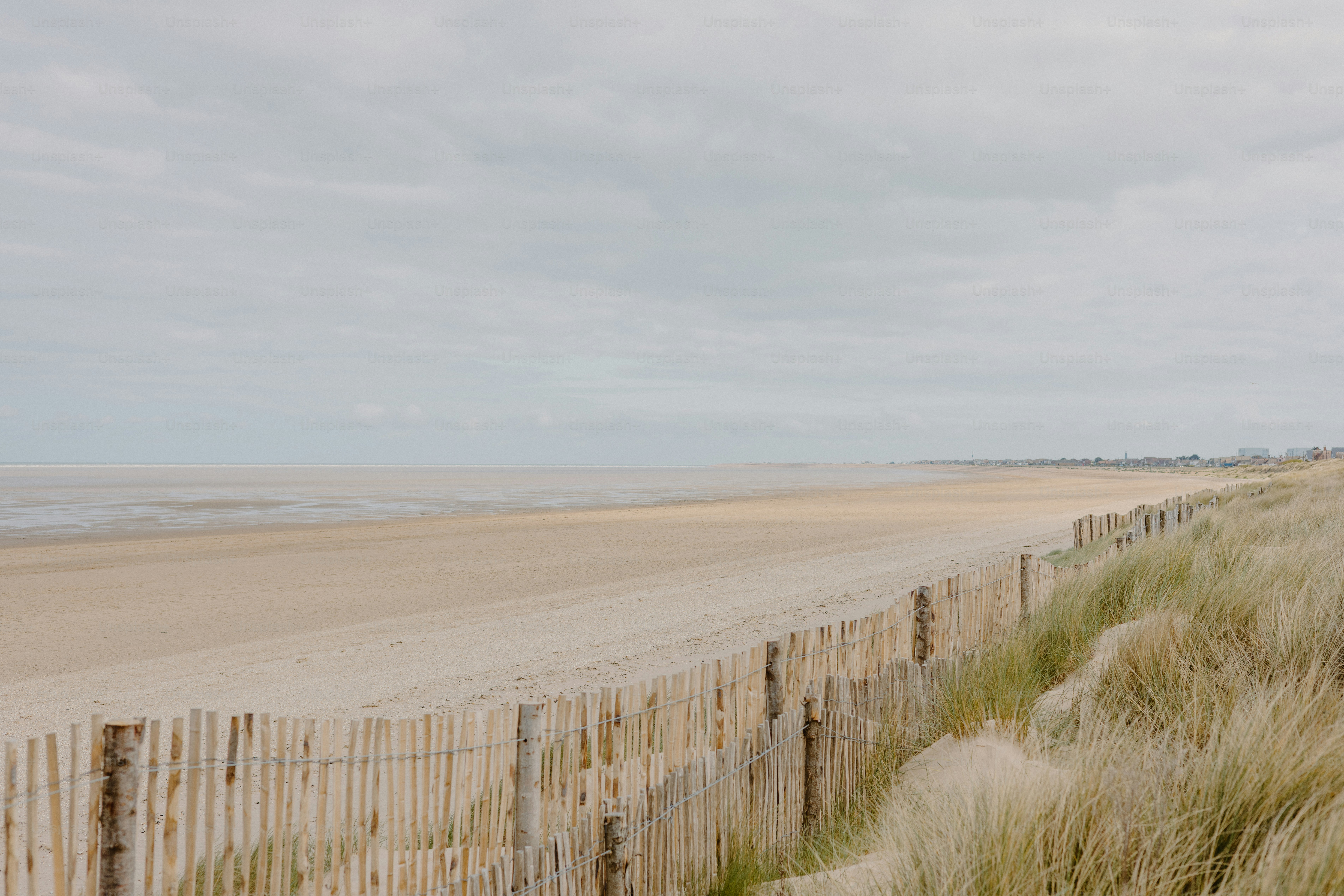 Sandy beach with a wooden fence and grass.
