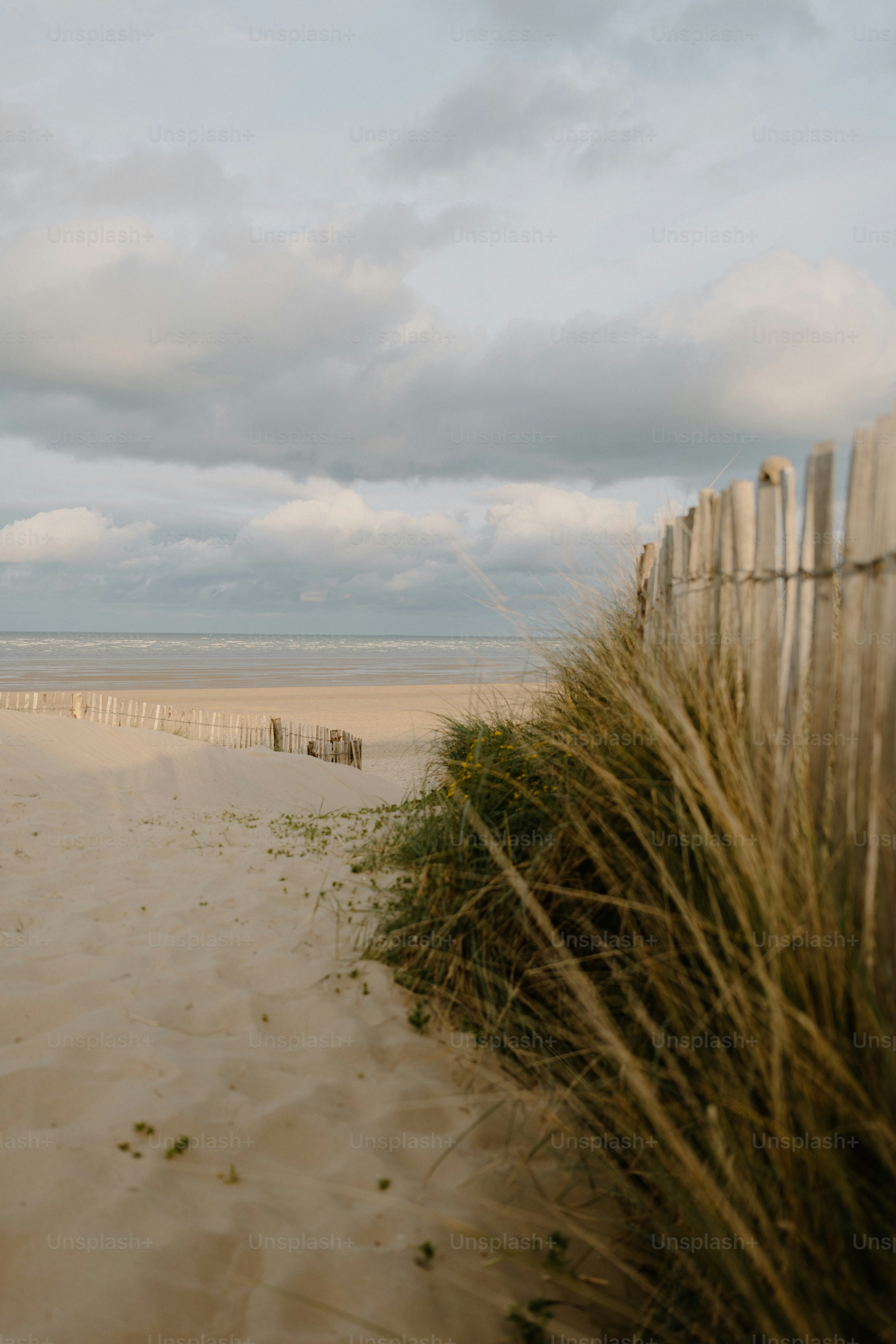 Sandy beach with a fence and cloudy sky.