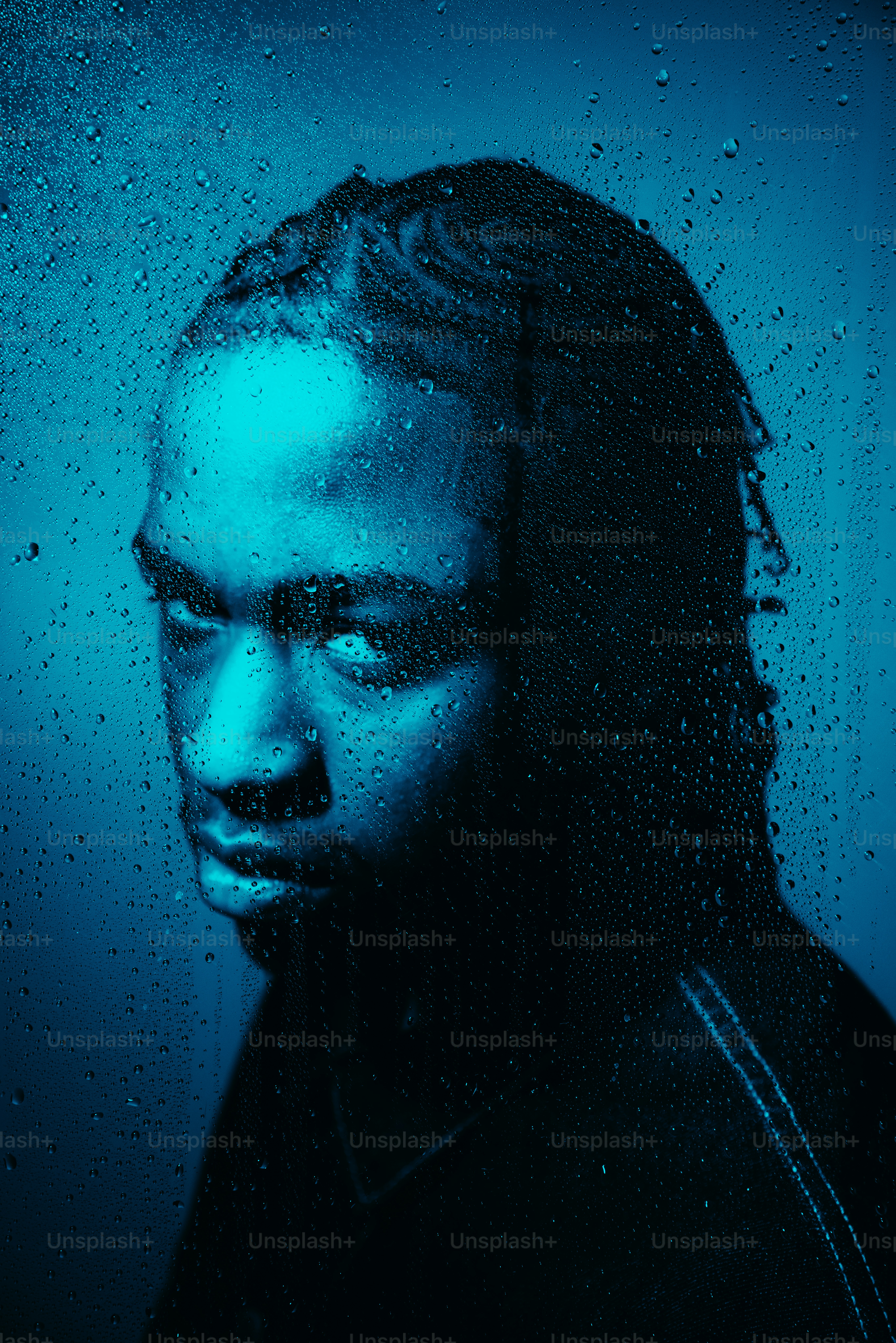 A man is illuminated behind rain-streaked glass.