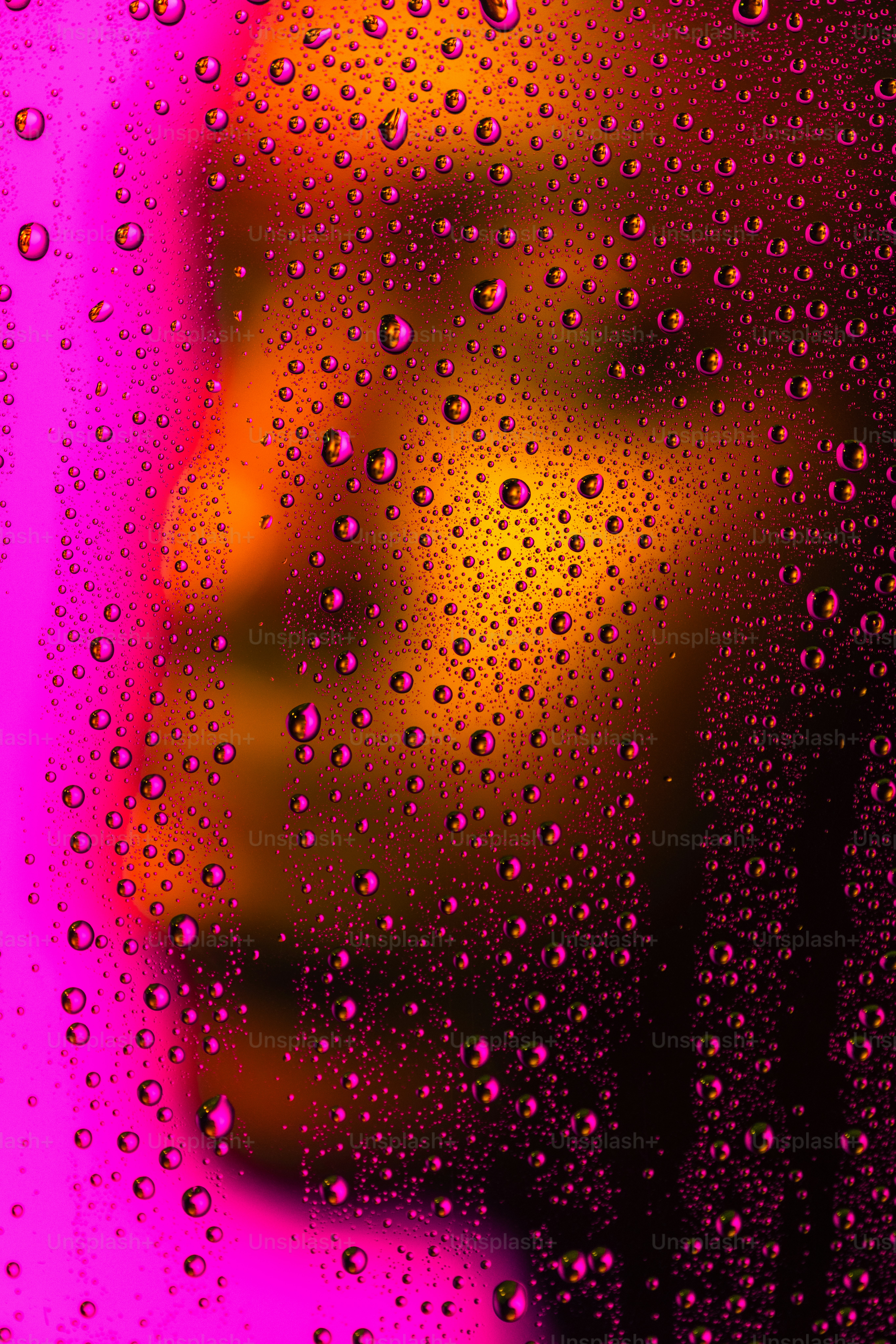 Droplets on a surface reflect vibrant pink and gold.