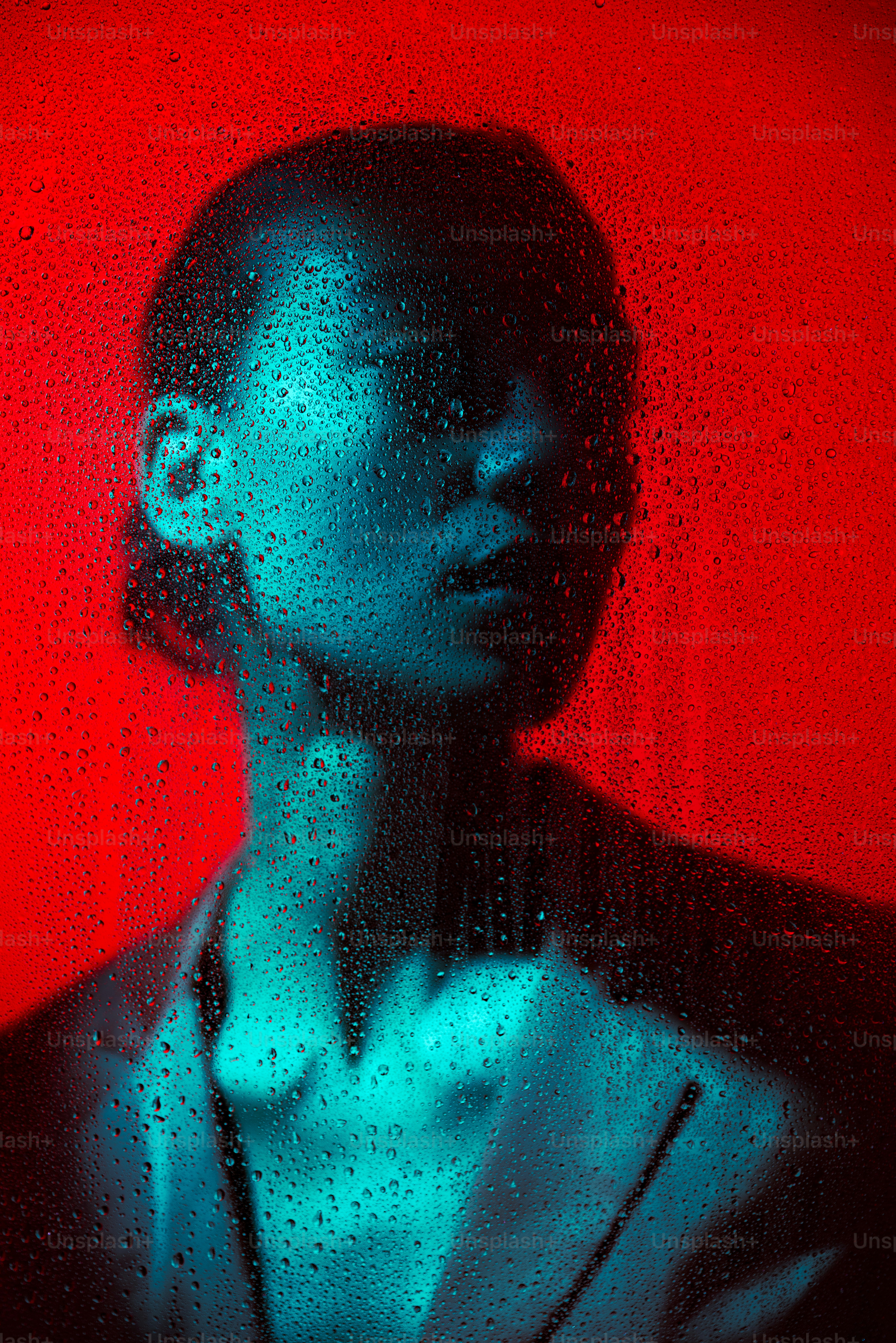 Una persona está de pie detrás de un vidrio mojado con fondo rojo.