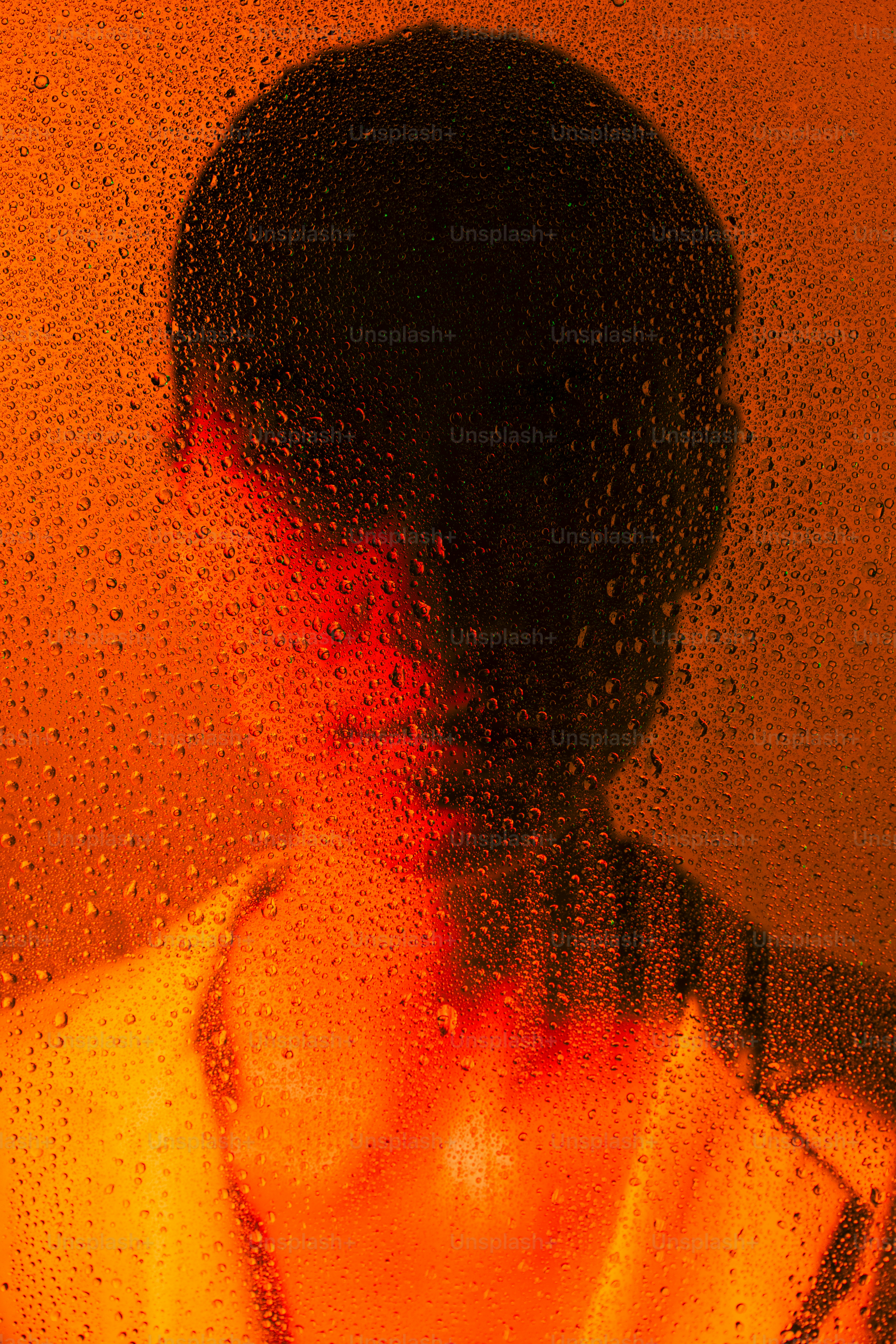 A person is behind wet glass, lit by orange.