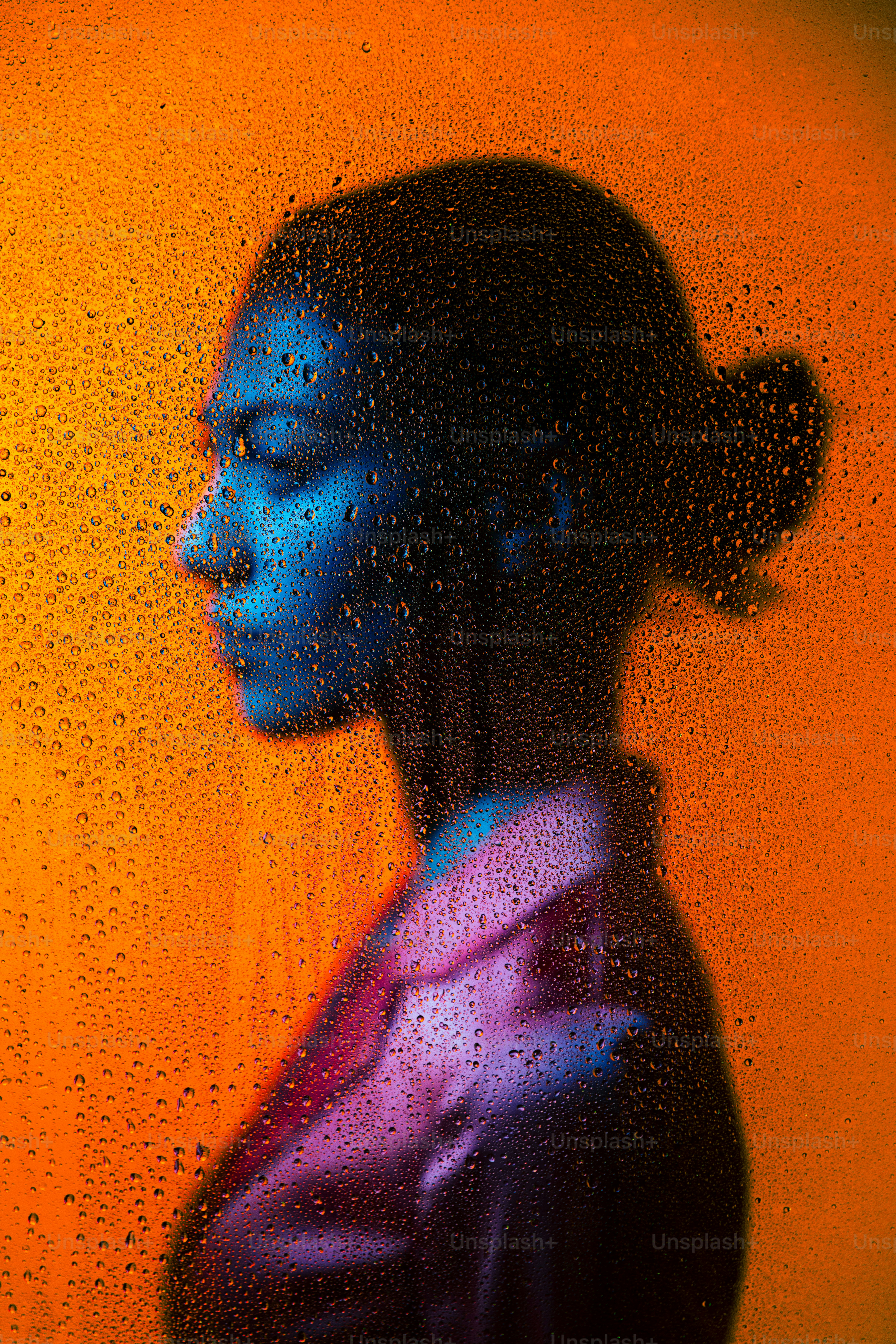 Woman's profile behind glass with droplets.