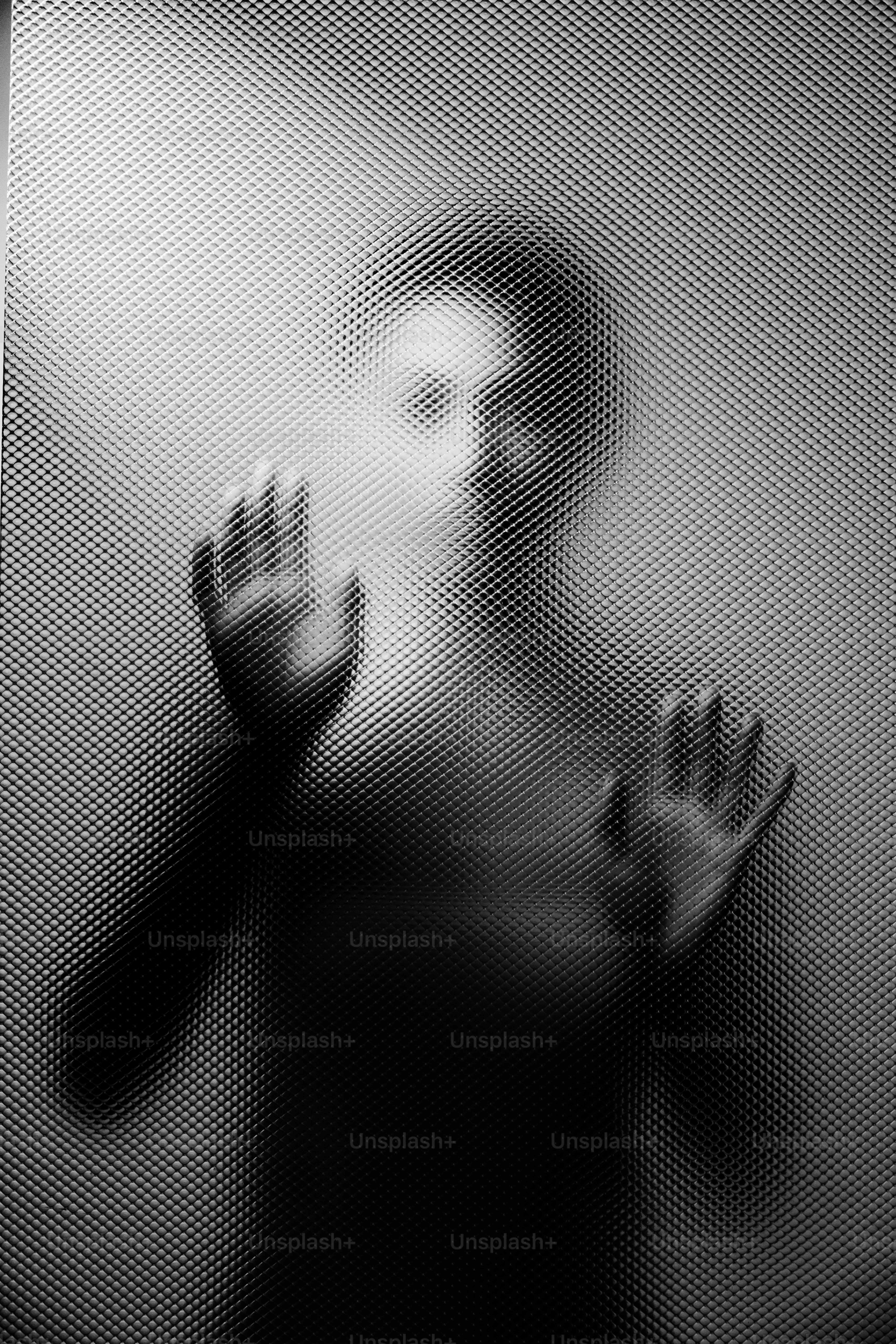 A figure presses hands against textured glass.