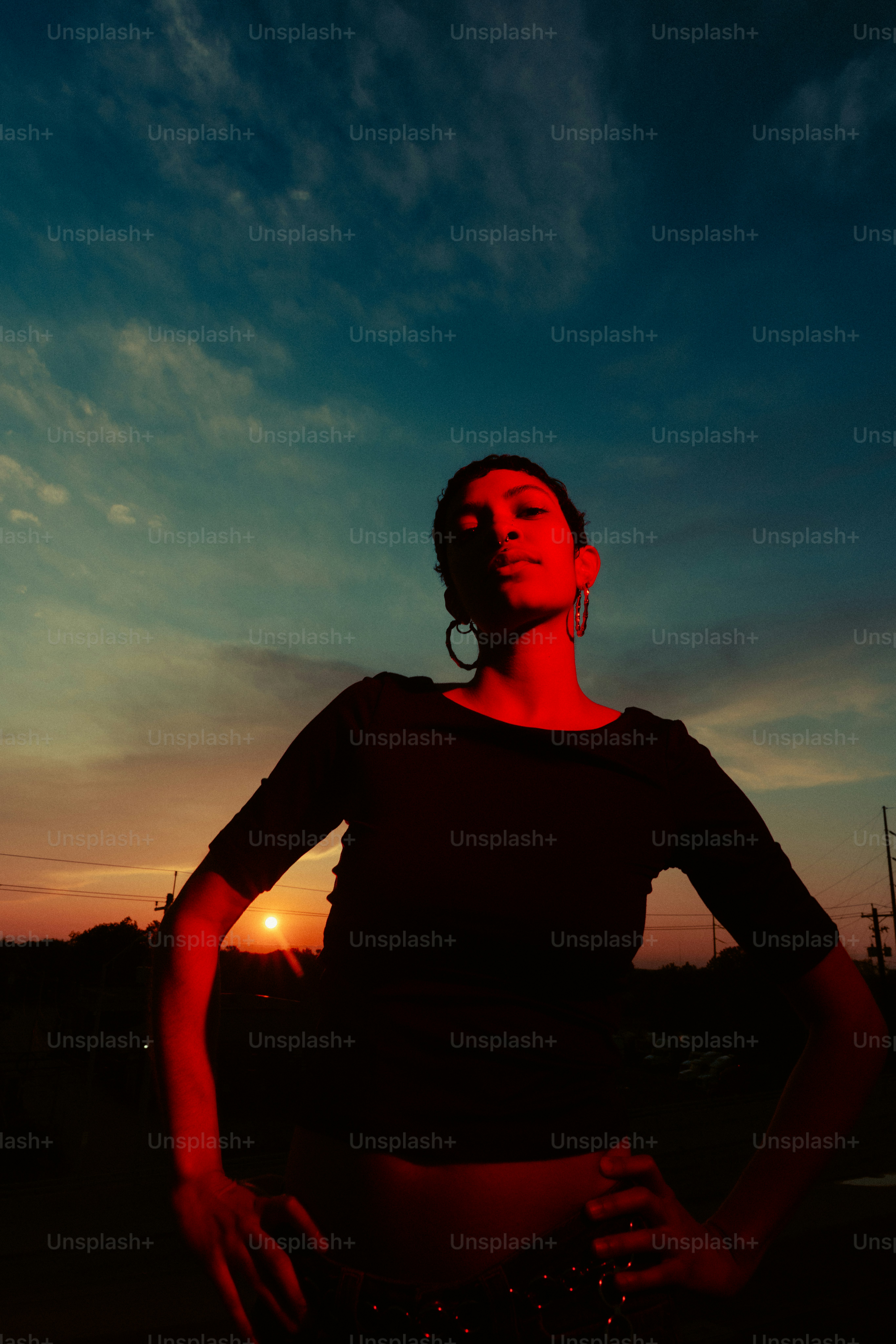 Woman poses confidently with a fiery sunset backdrop.