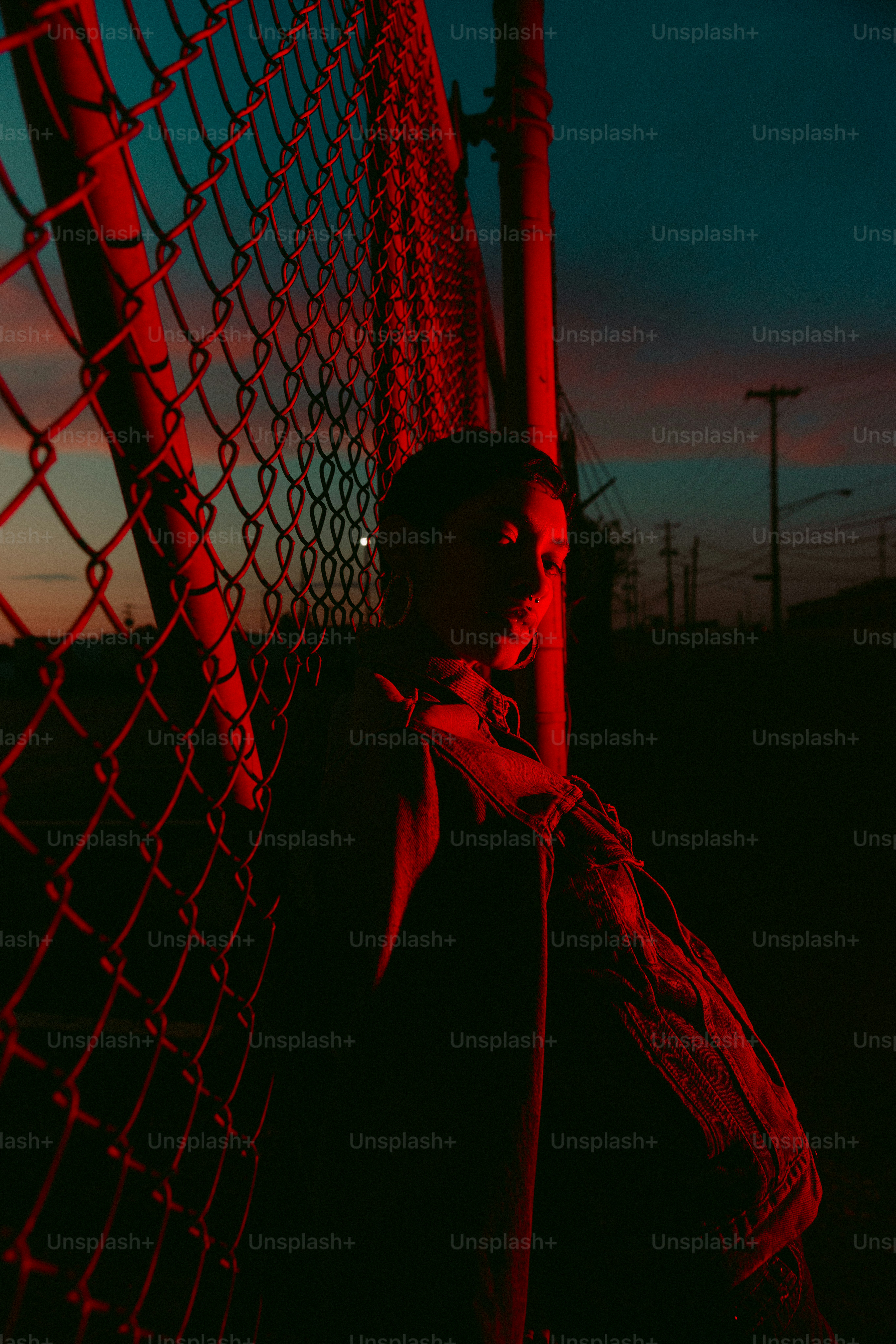 A person leans against a fence, lit red.