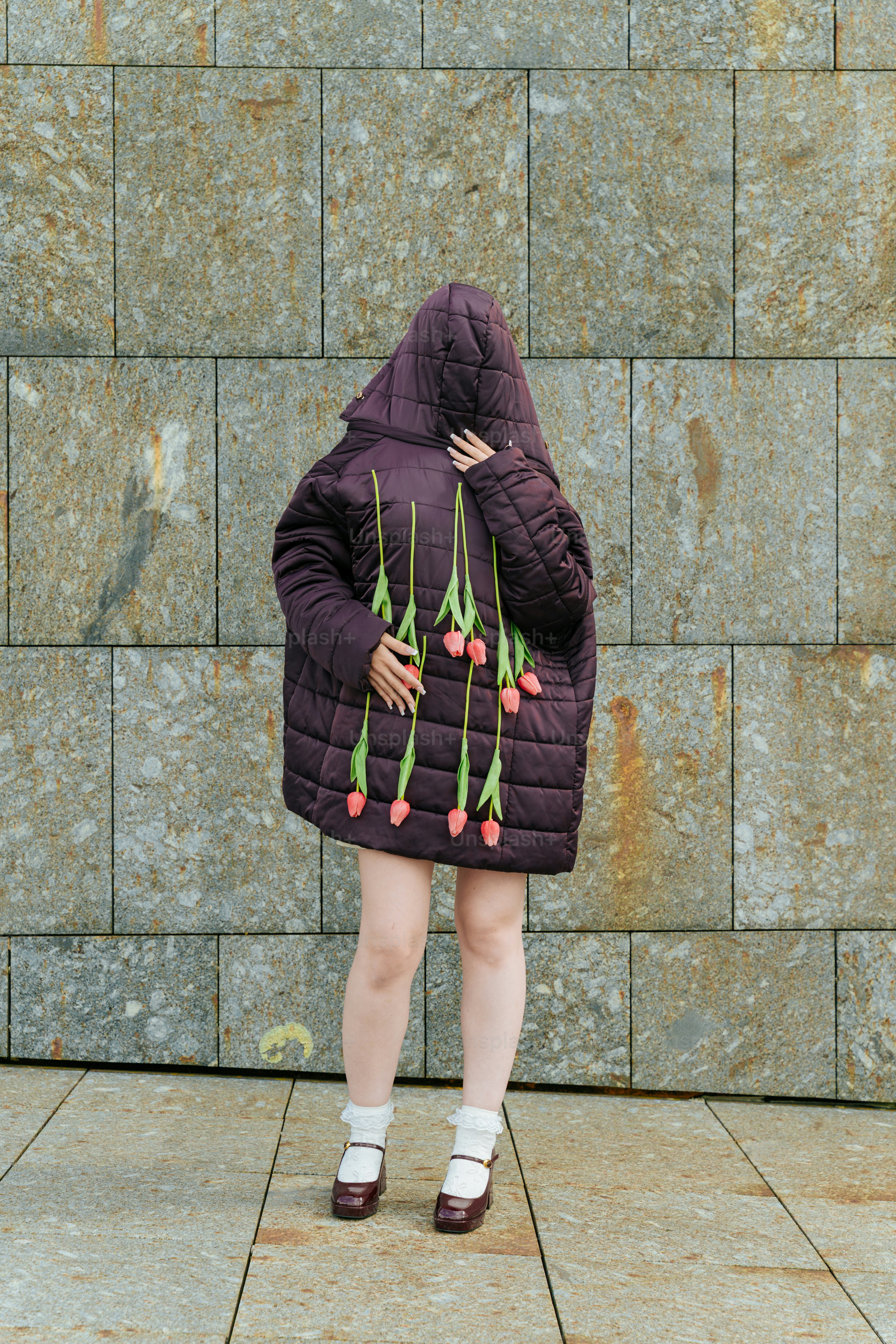 Person im Mantel hält Tulpen vor eine Wand.