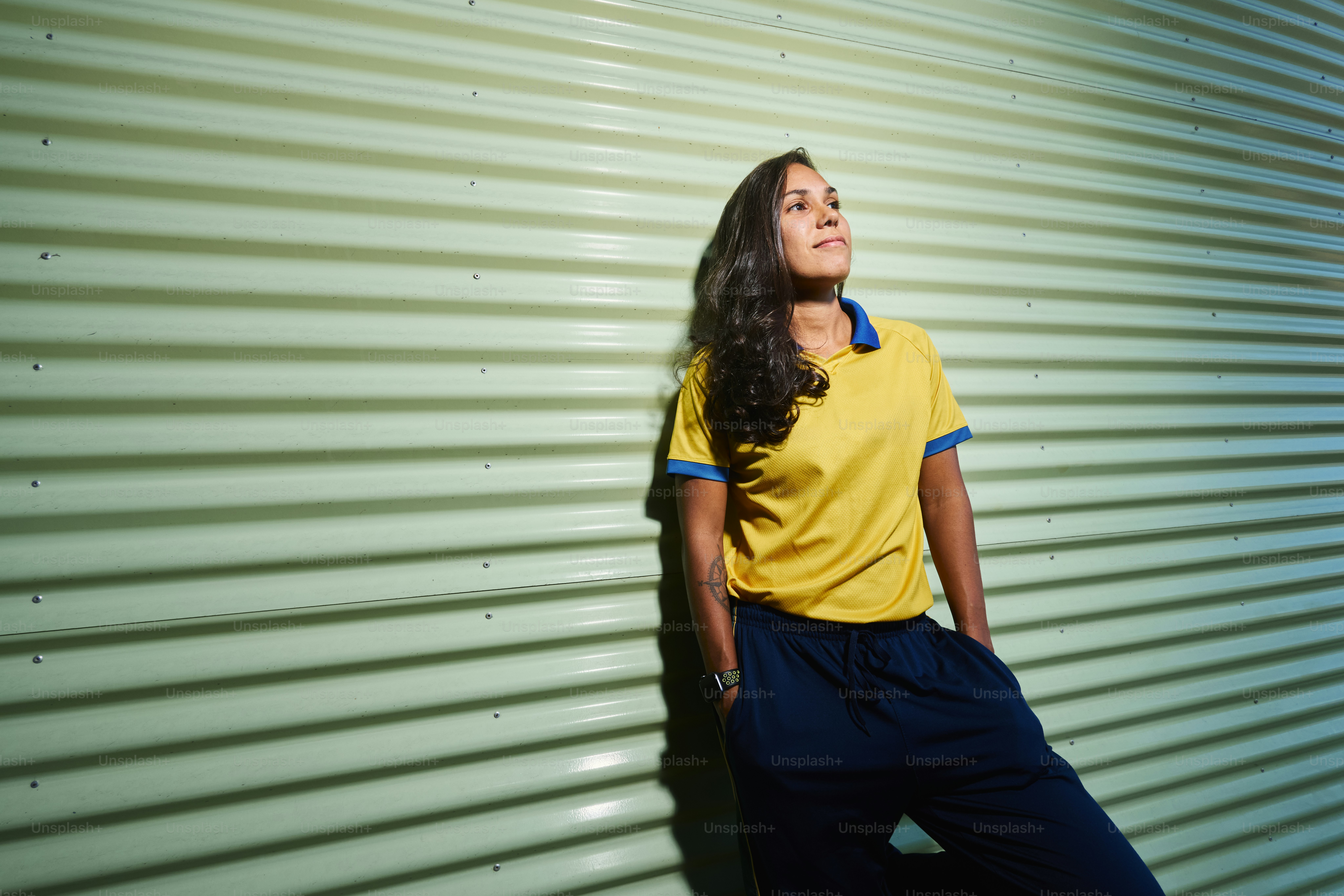 Woman in yellow shirt leaning on a wall.