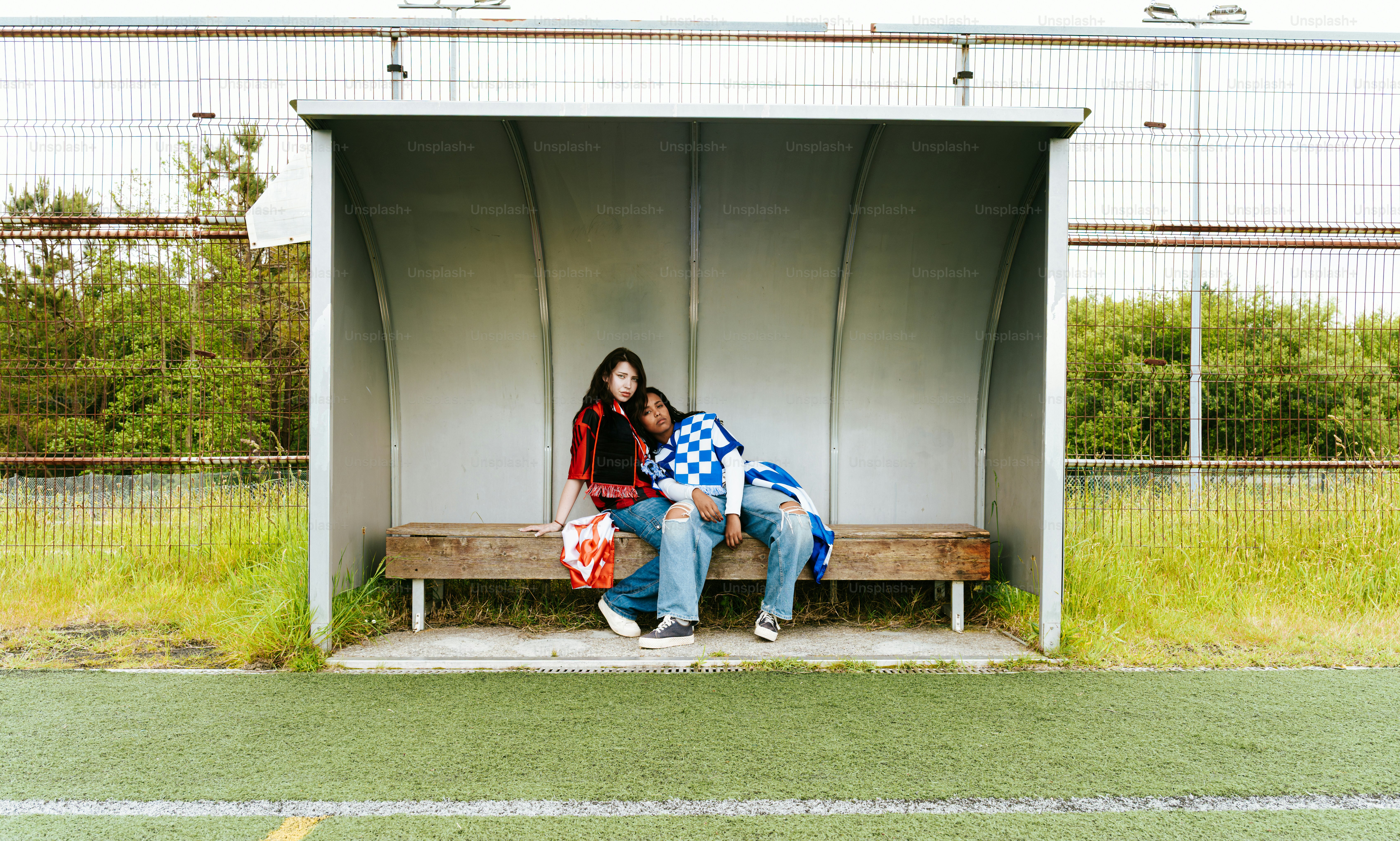 Two people sit on a bench under a shelter.