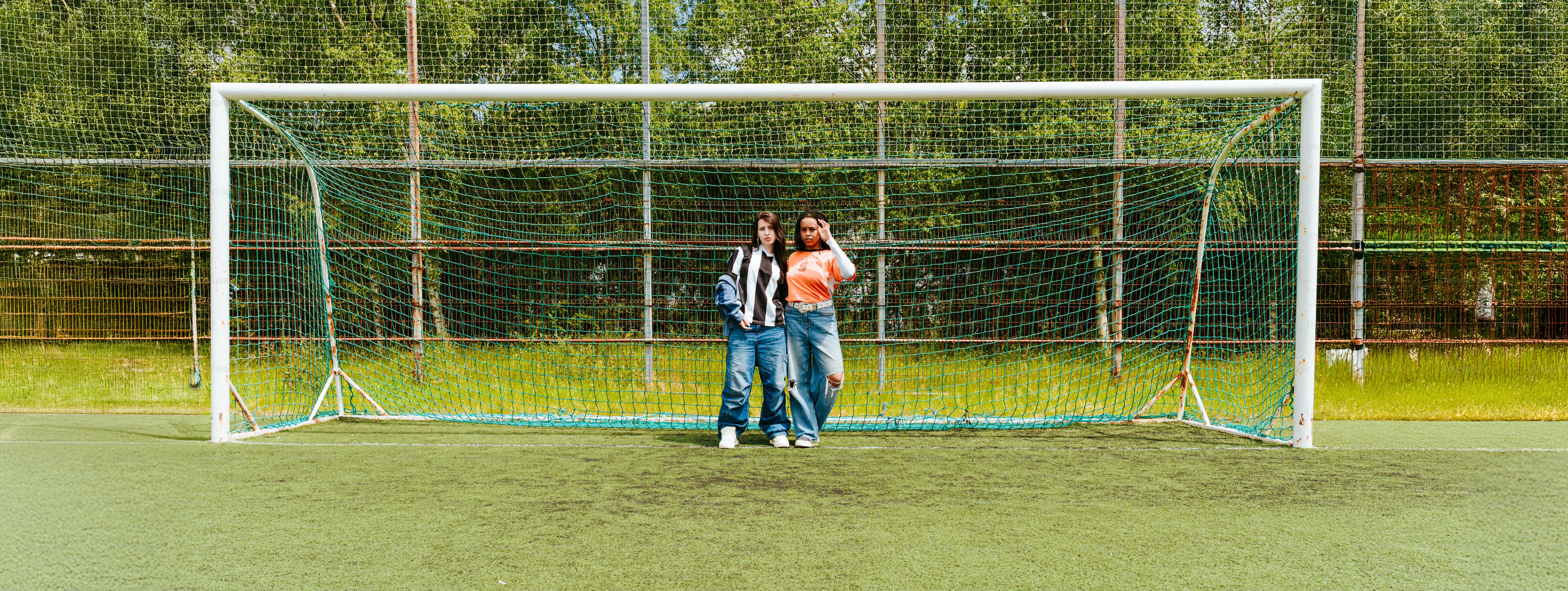 Two people stand in front of a soccer goal.
