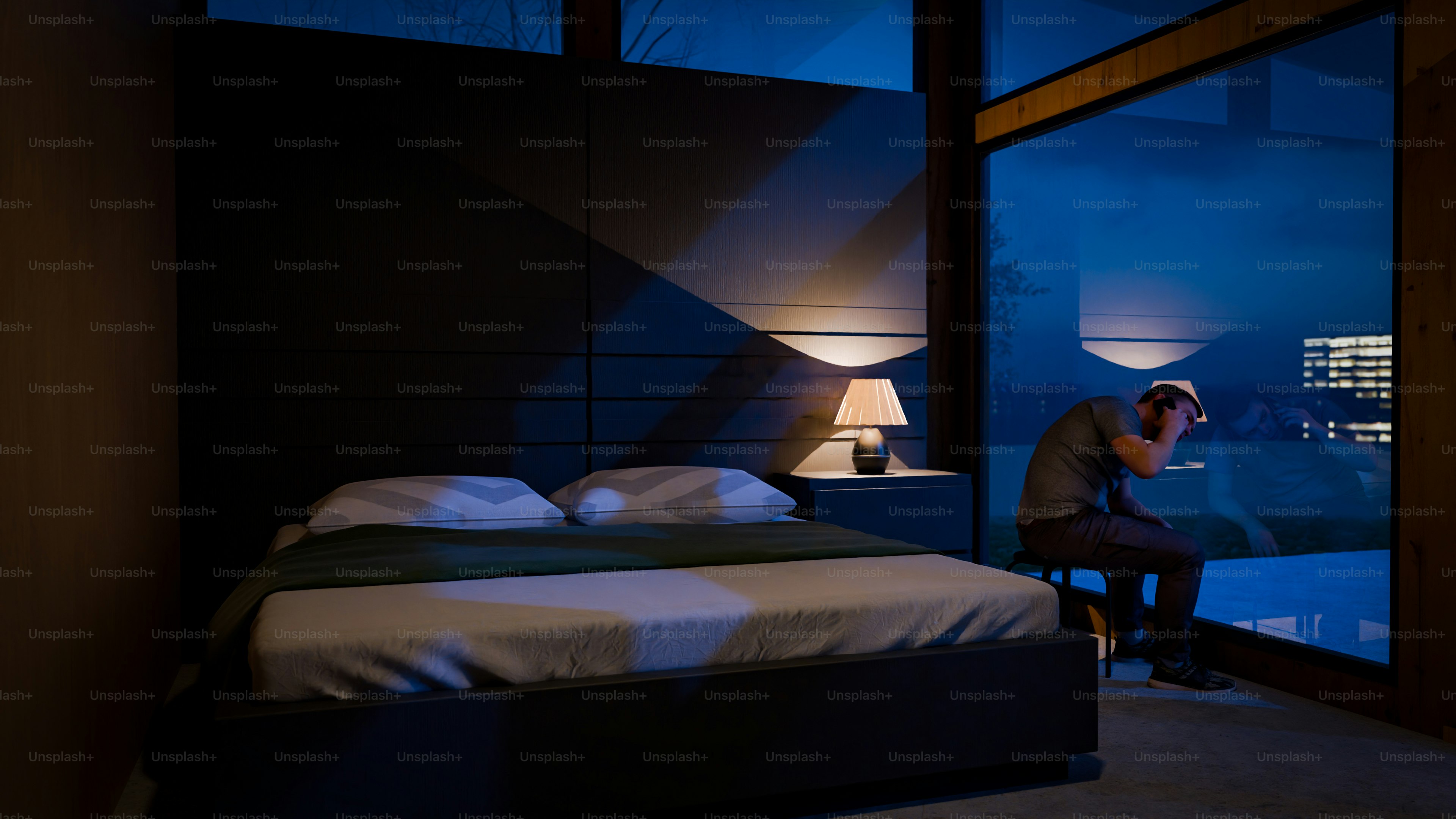 A man sits stressed in a dark bedroom.