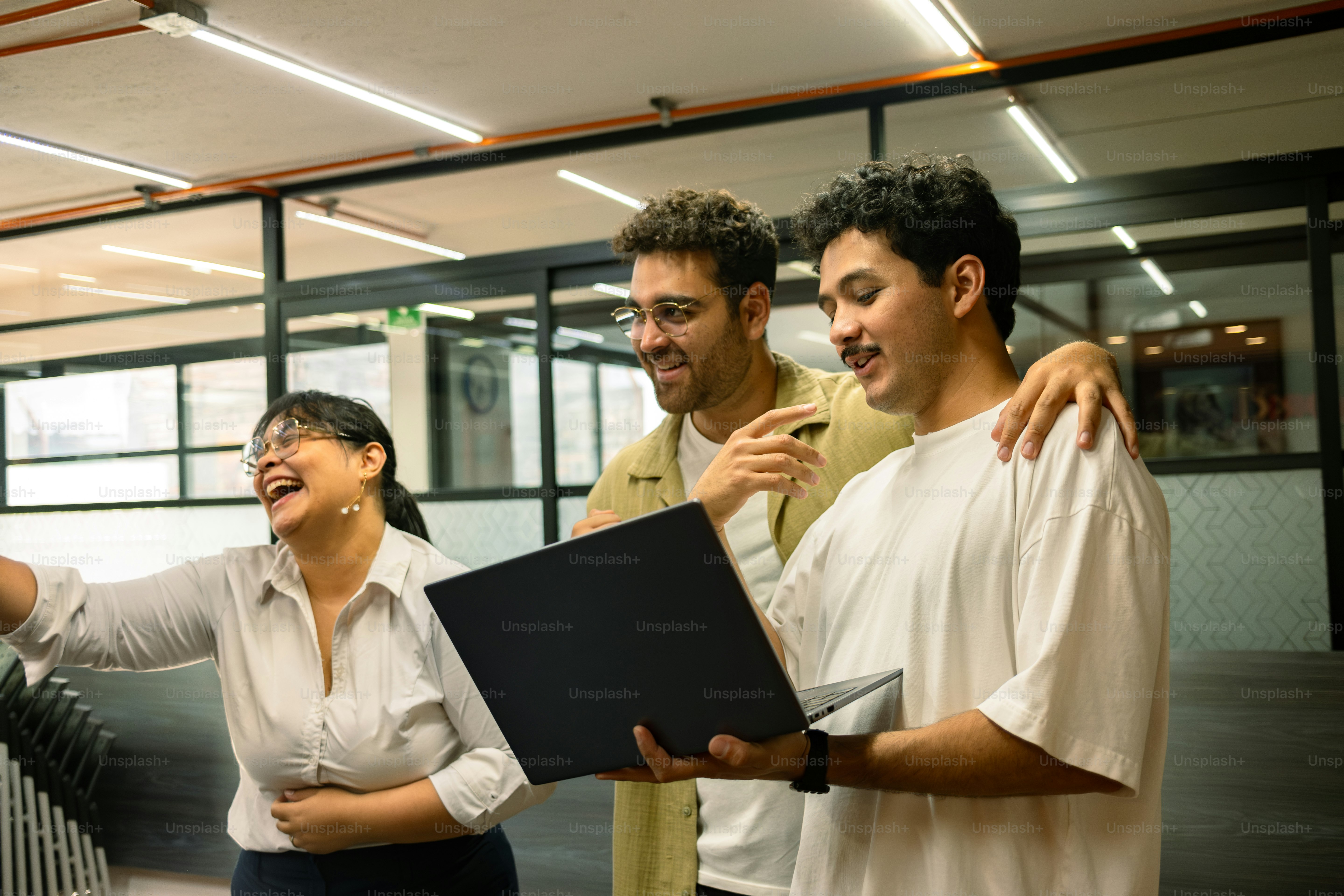Three colleagues share a laugh while working on a laptop.