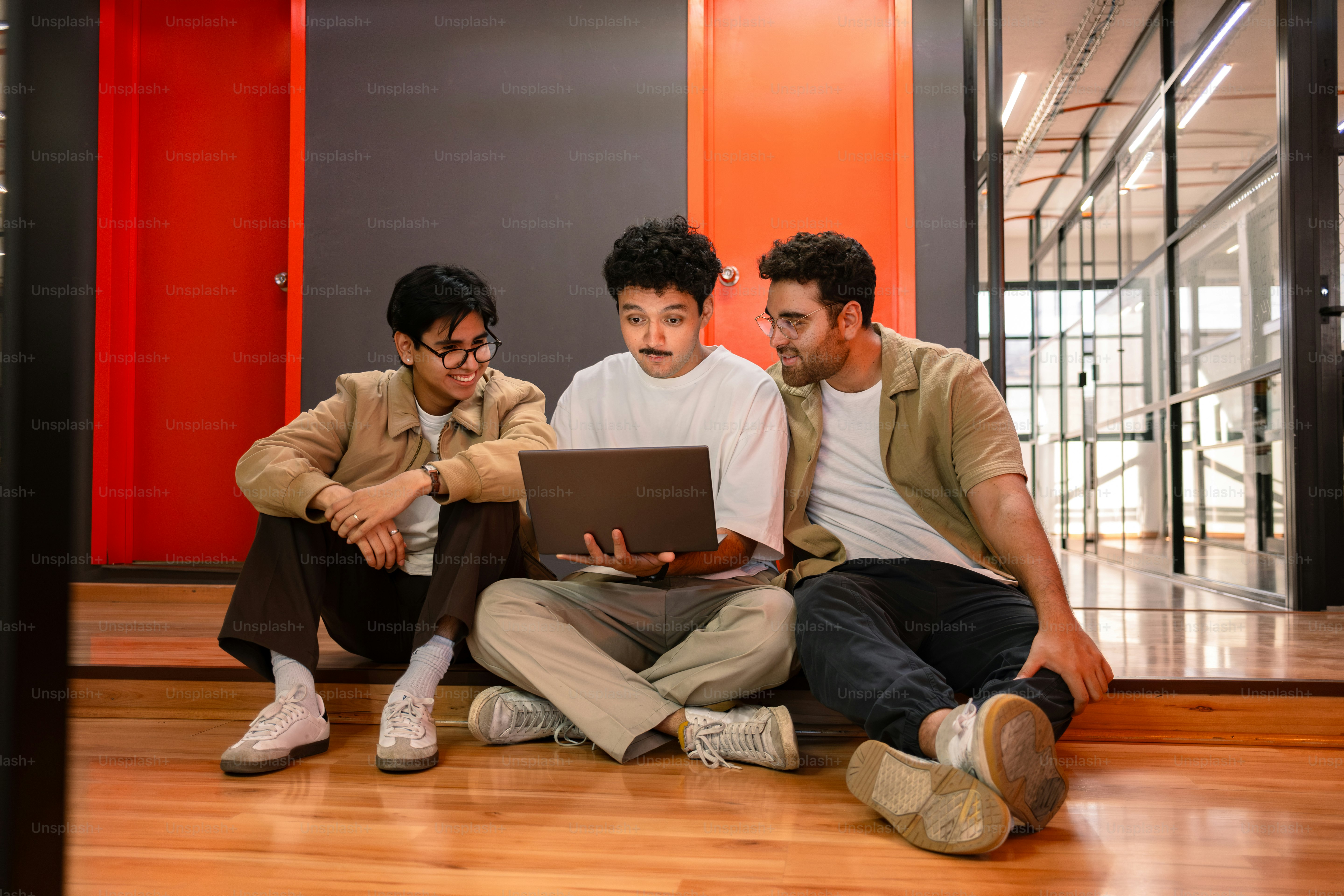 Three men collaborate while looking at a laptop.