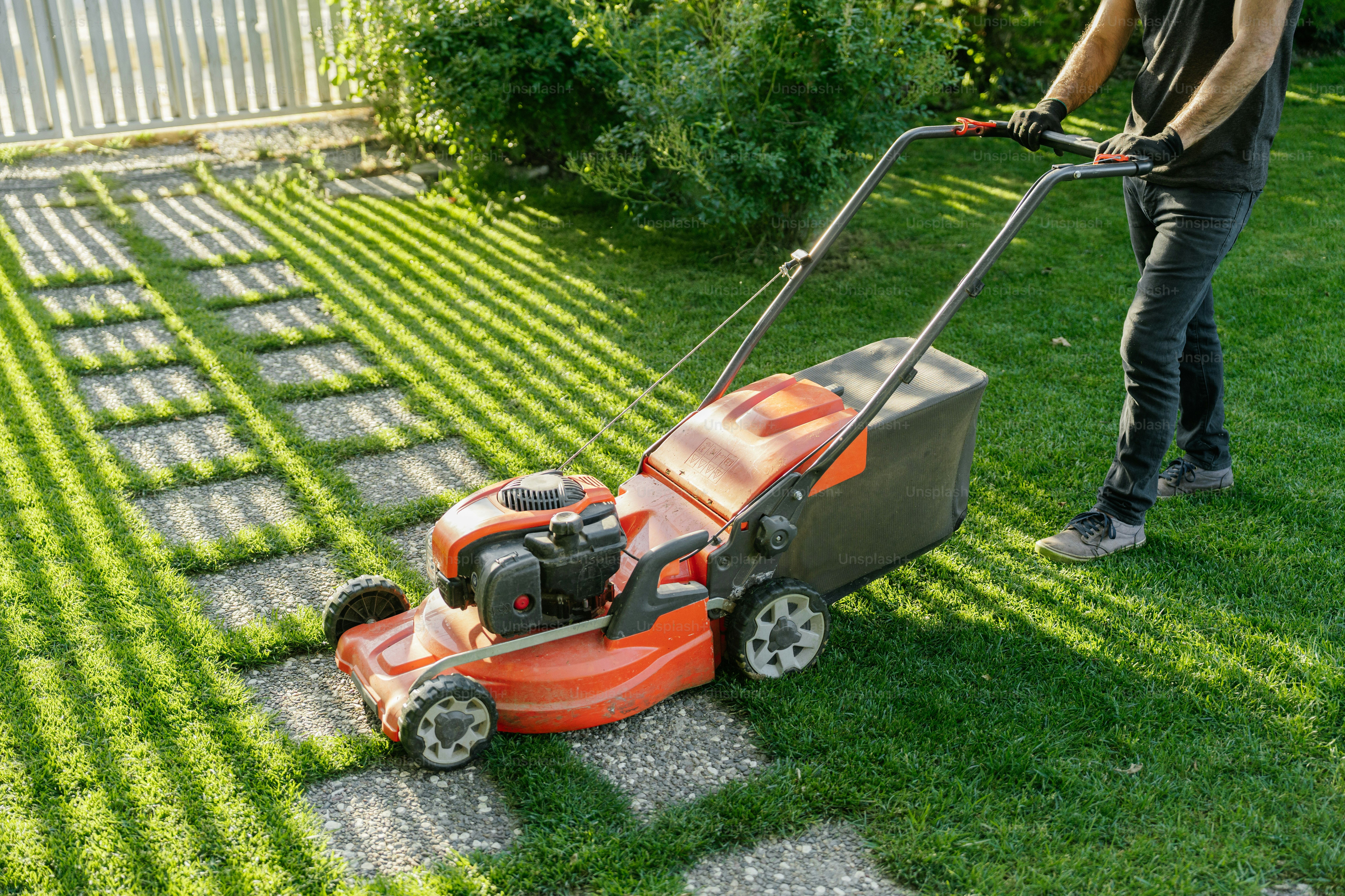 Man is mowing the lawn with a red mower.