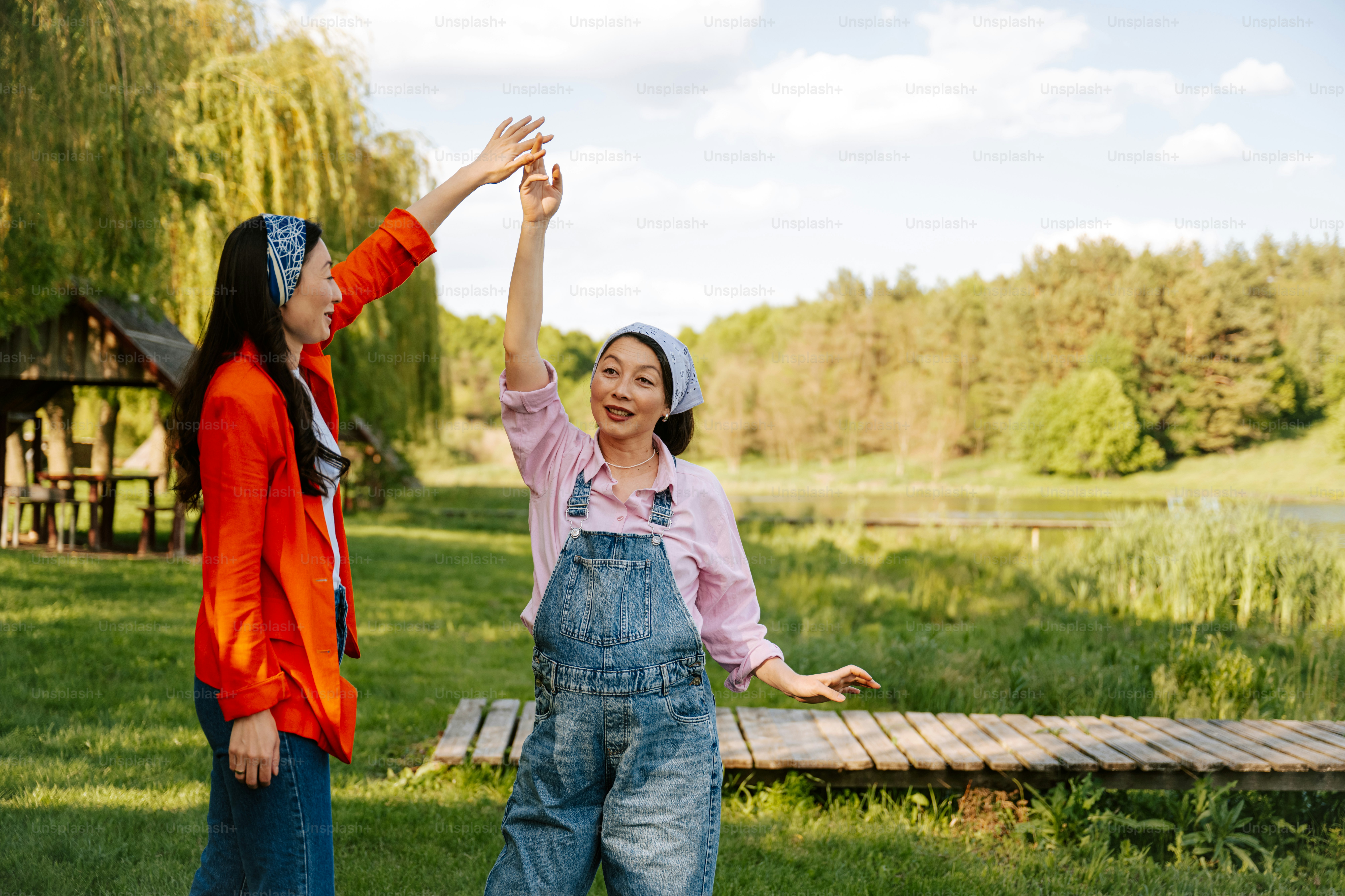 Two women are dancing happily outdoors on a sunny day.