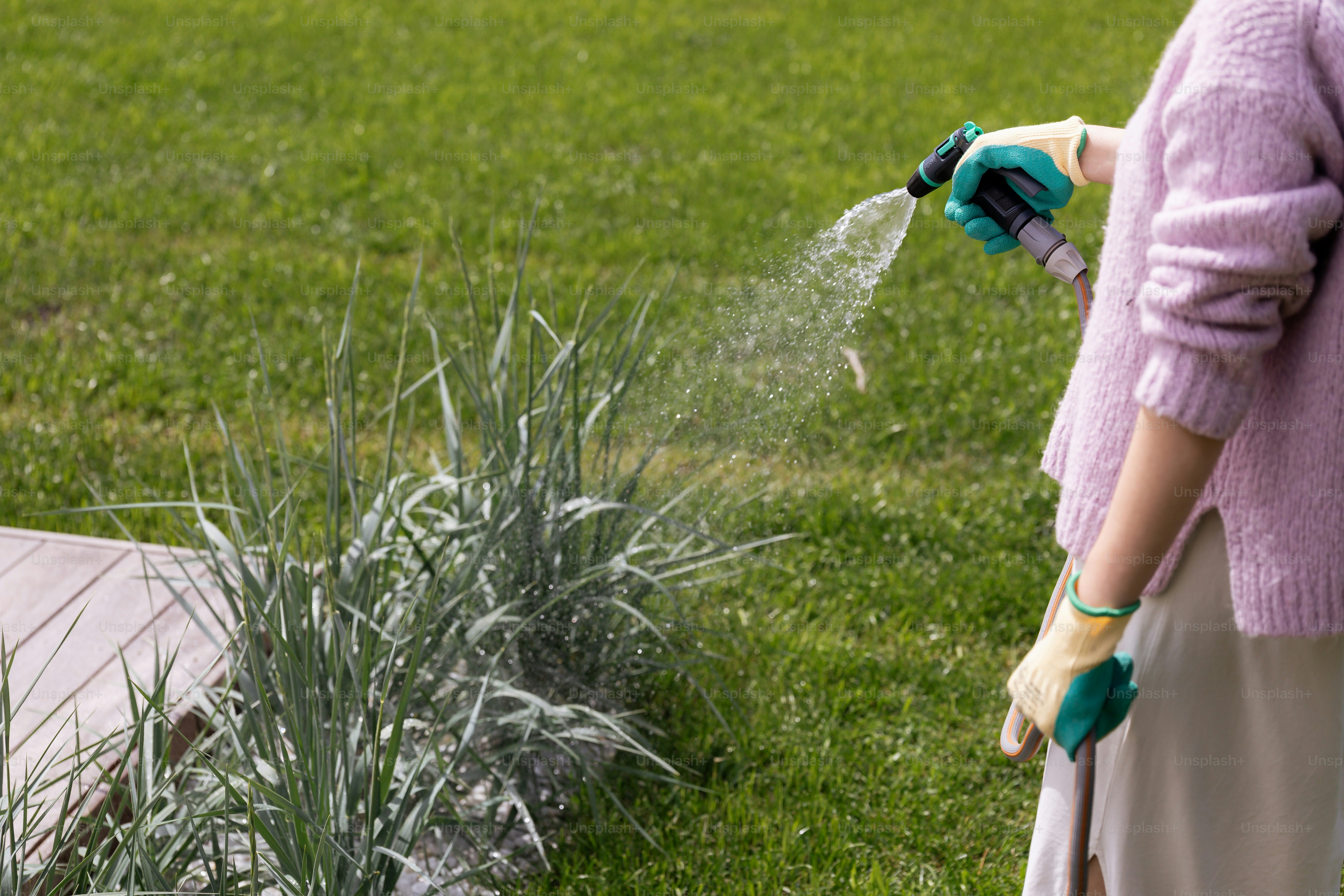Woman waters plants with a hose in the yard.