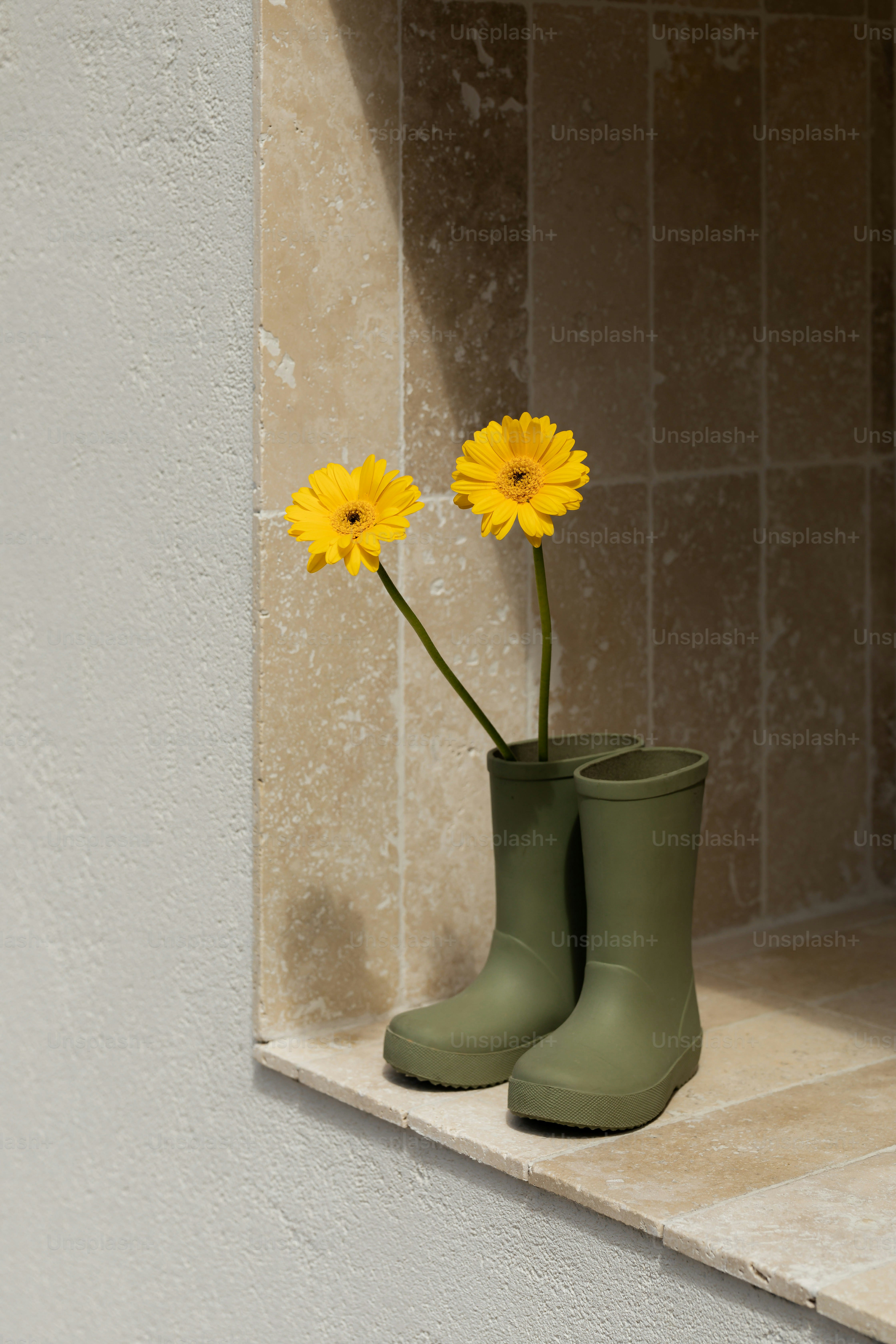 Two yellow flowers bloom in green rain boots.