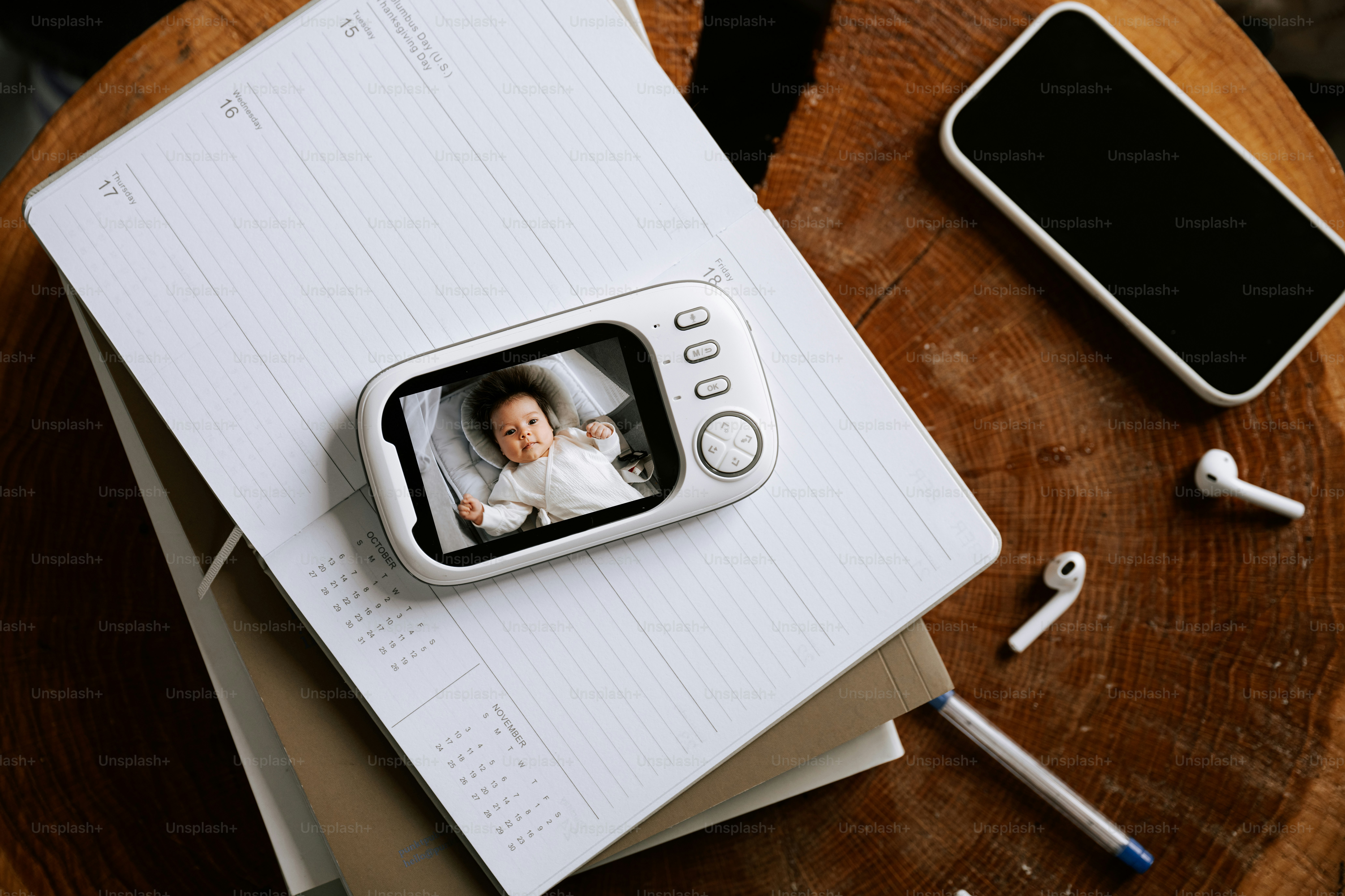 Baby monitor, phone, and notebook on a table.