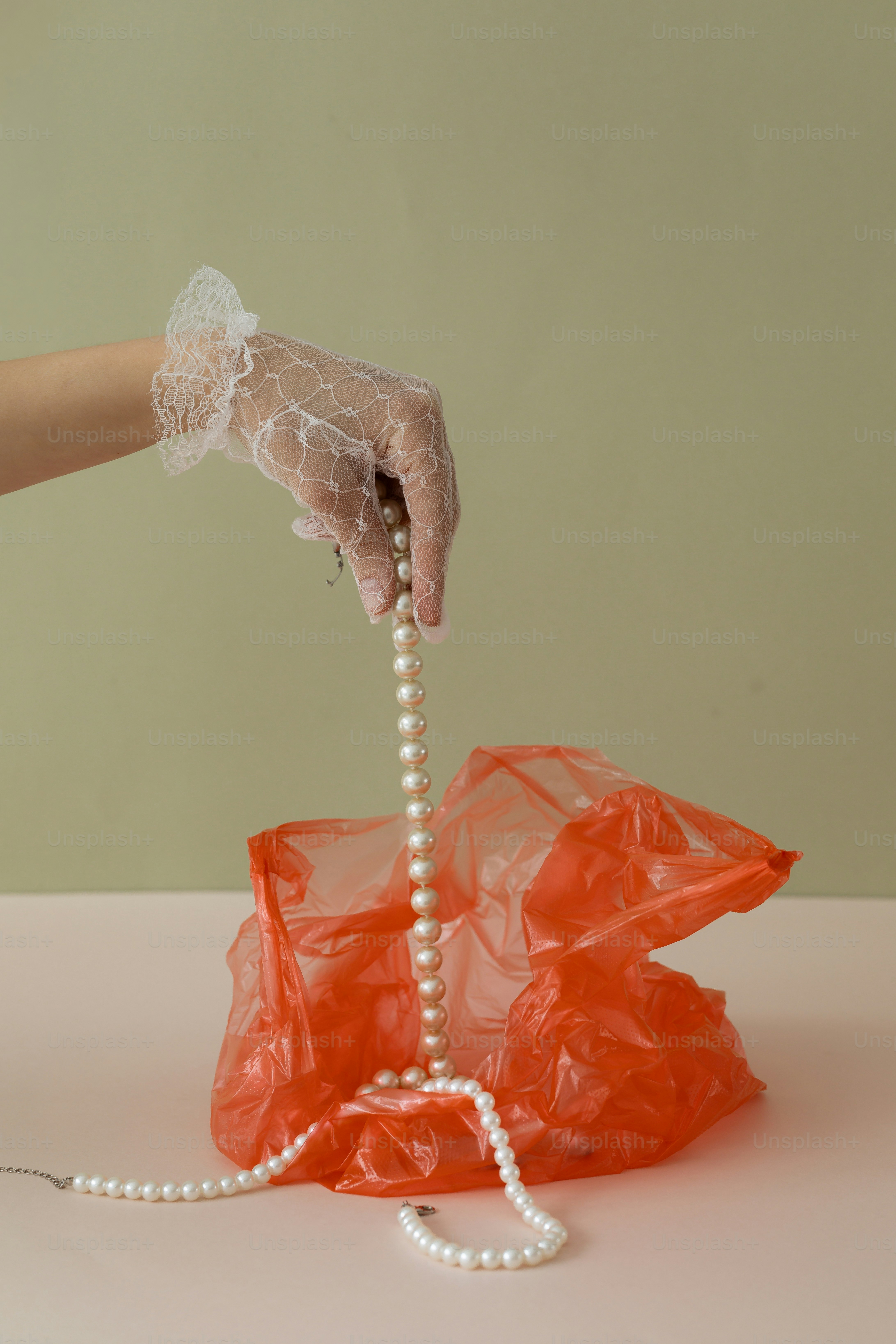 A hand in a glove lifts pearls from a bag.
