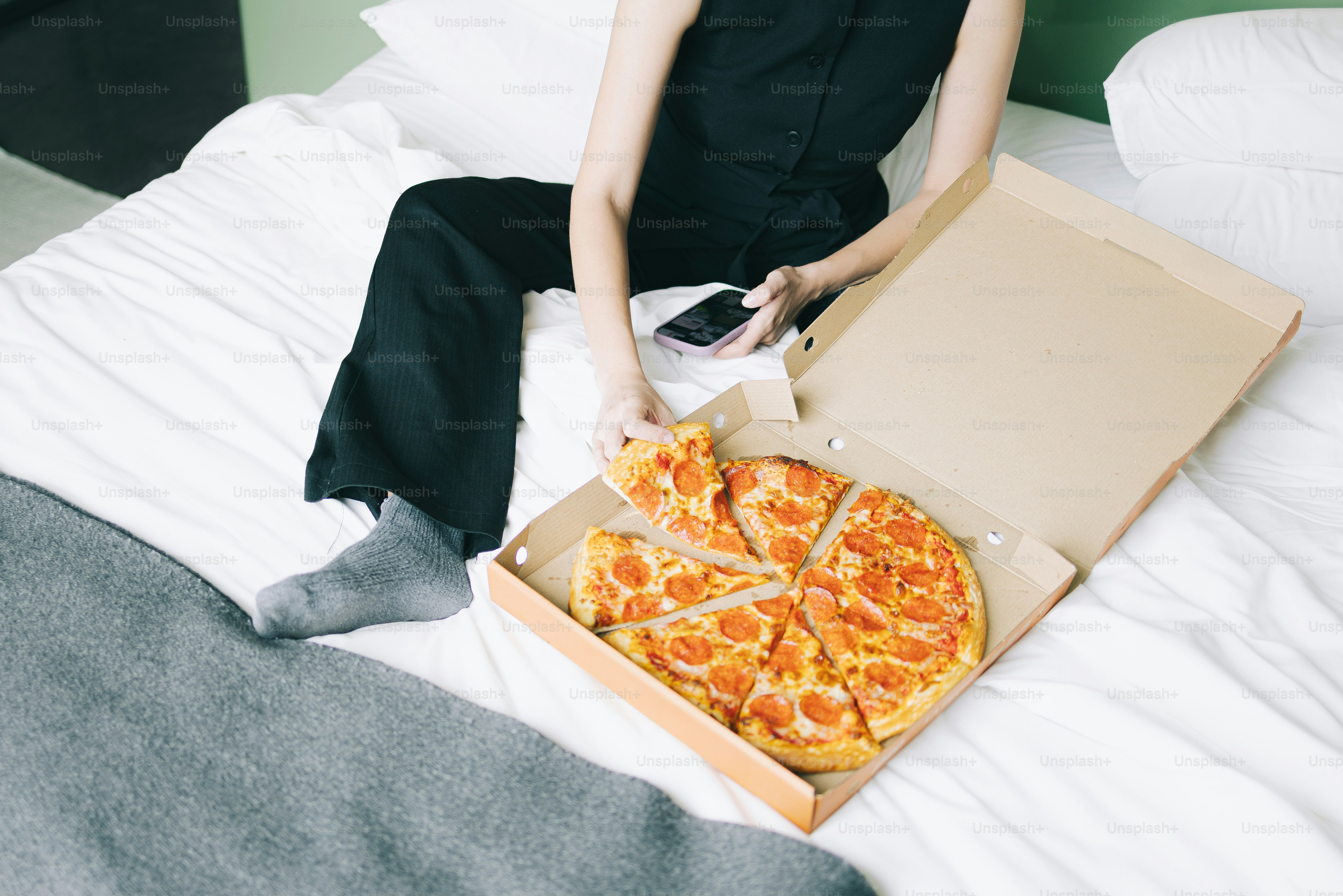 Pizza on a bed with someone enjoying a slice.