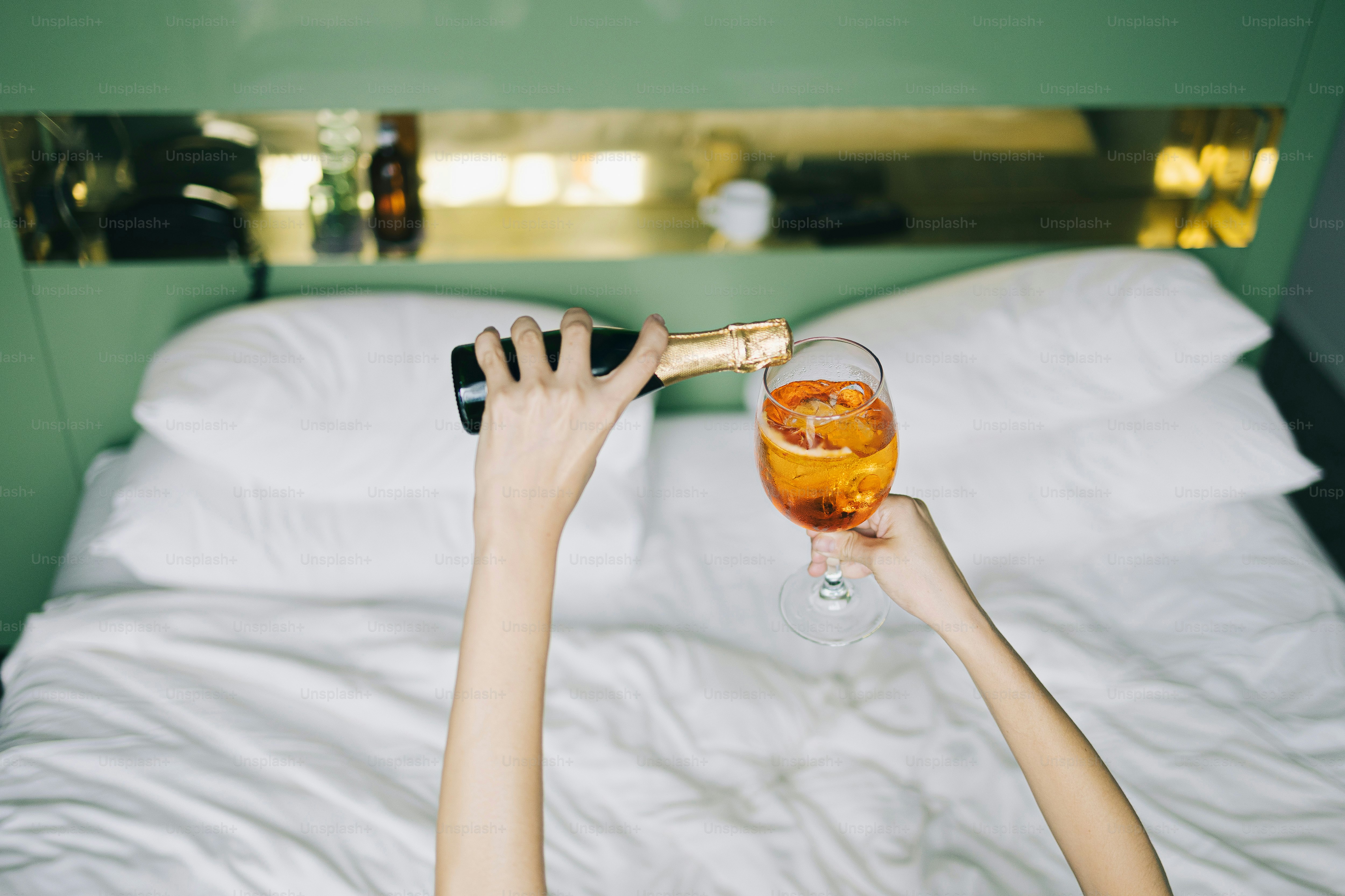 Pouring champagne into a glass on a bed.